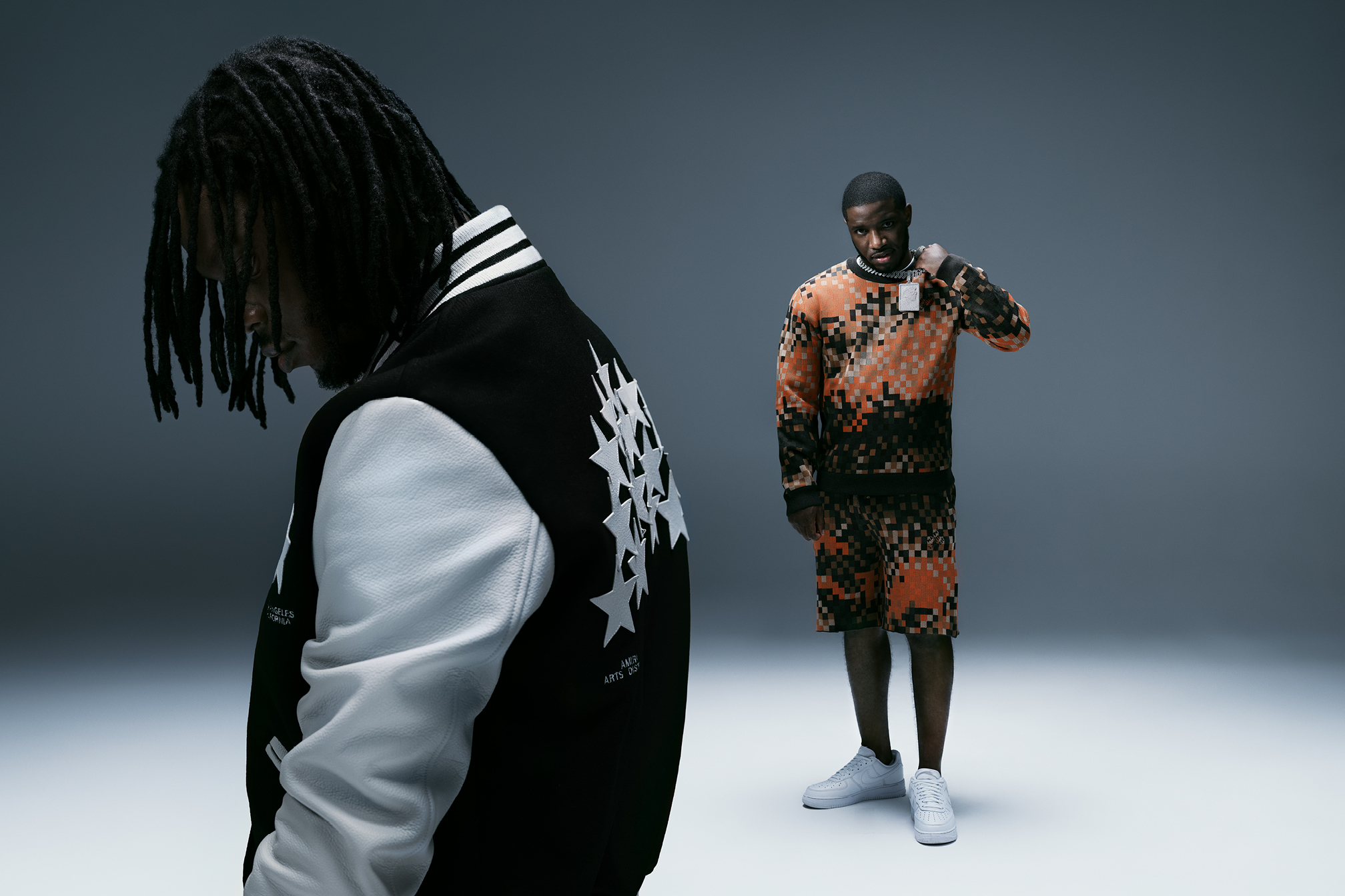 Two individuals wearing bold, graphic fashion featuring geometric patterns and stripes in contrasting black, white, and orange colours.