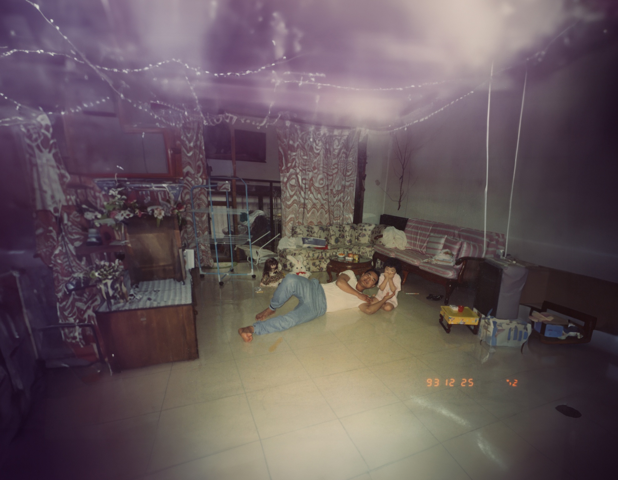 Interior room with purple walls, string lights on ceiling, person on floor in blue clothing, scattered furniture and belongings throughout.