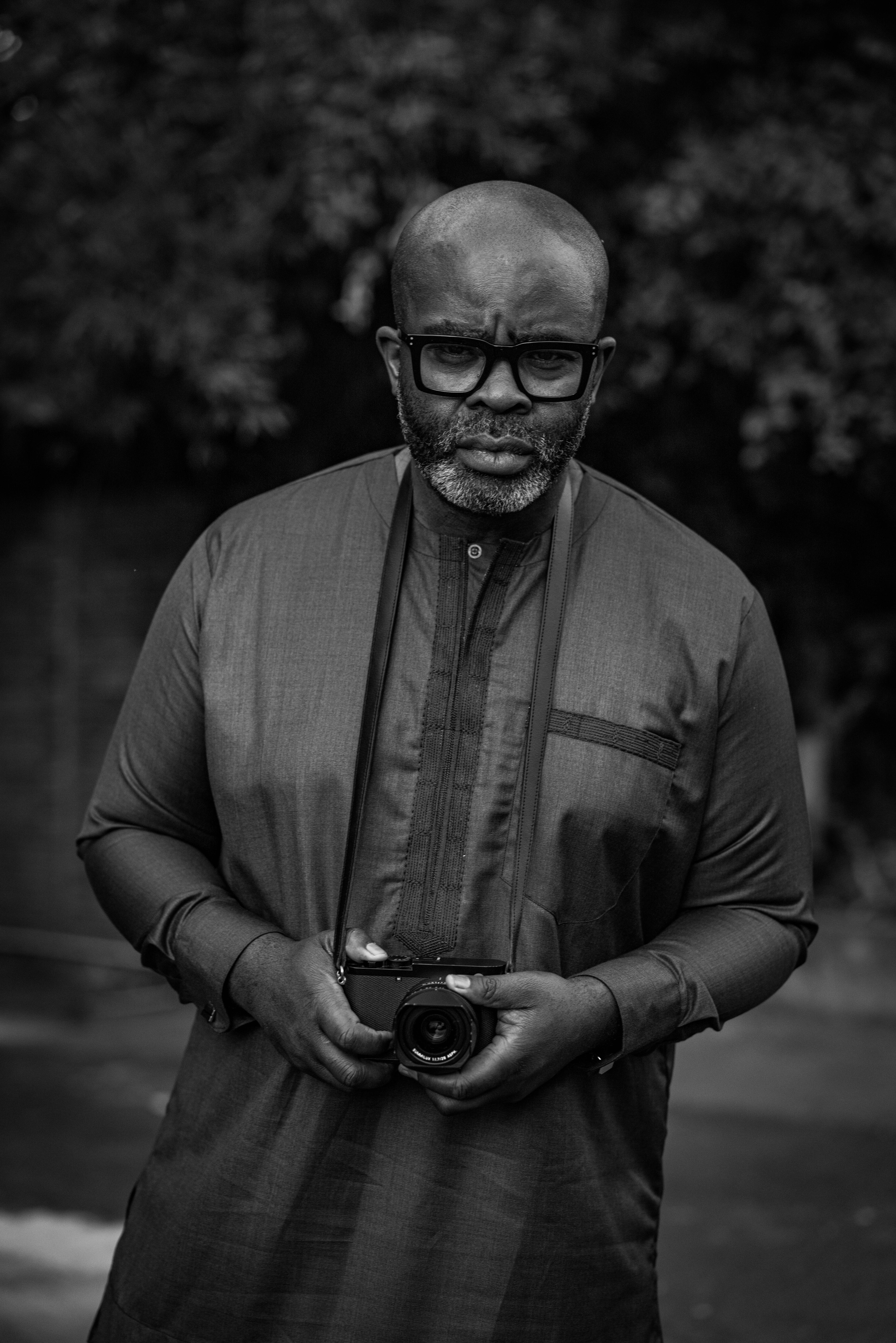 Elderly bearded man with glasses holding a camera, wearing a dark-coloured jacket.