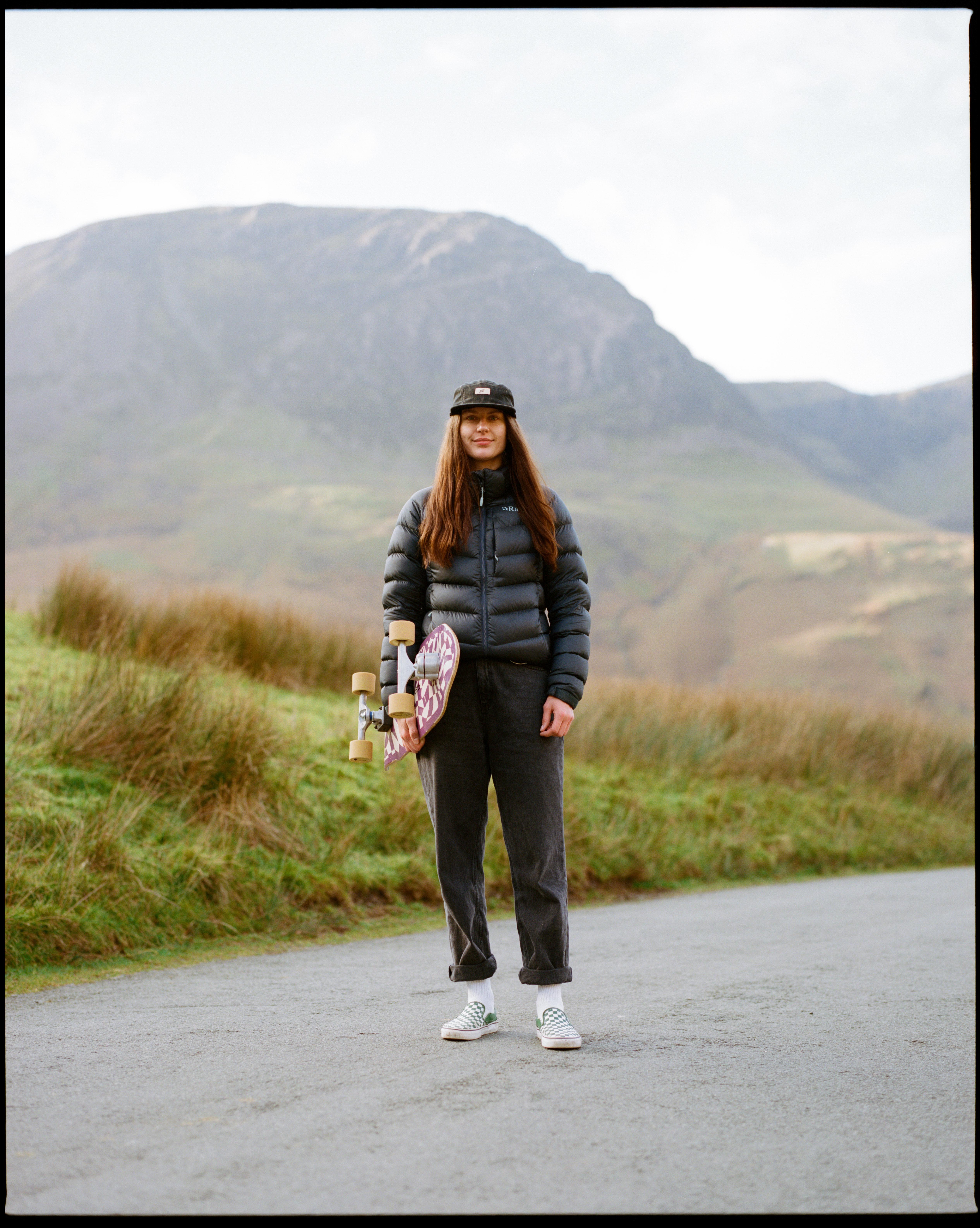 Woman in puffer jacket, hat, and trainers in countryside