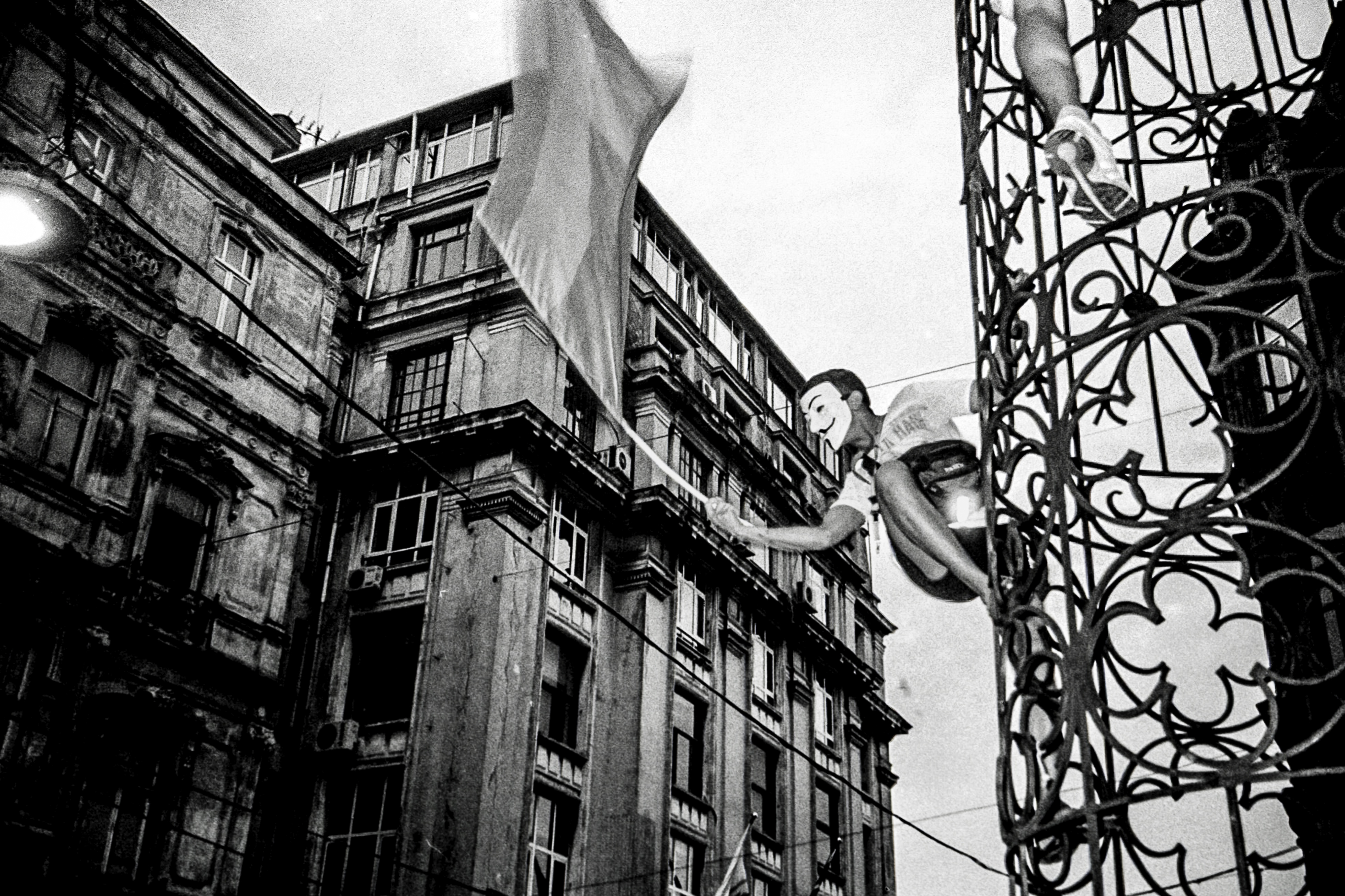 Monochrome image of an ornate building with balconies and a waving flag.