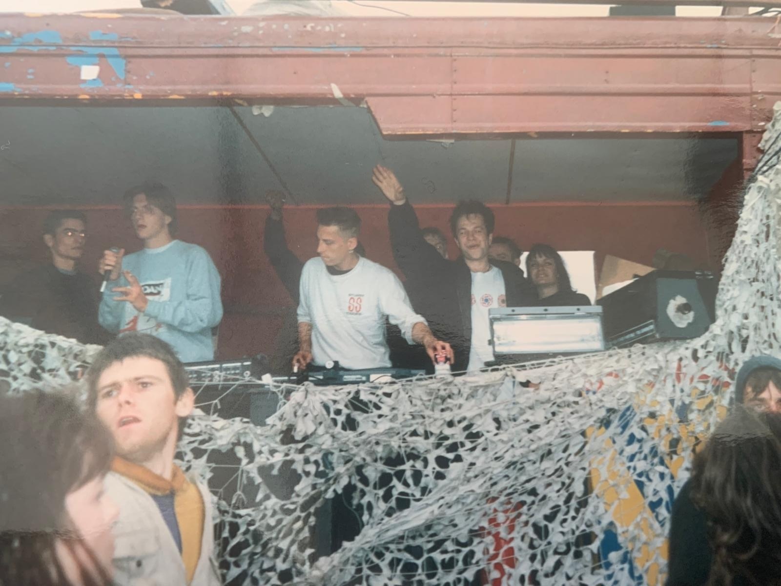 People in nightclub with DJ booth, scattered with white foam or artificial snow covering foreground and surfaces.