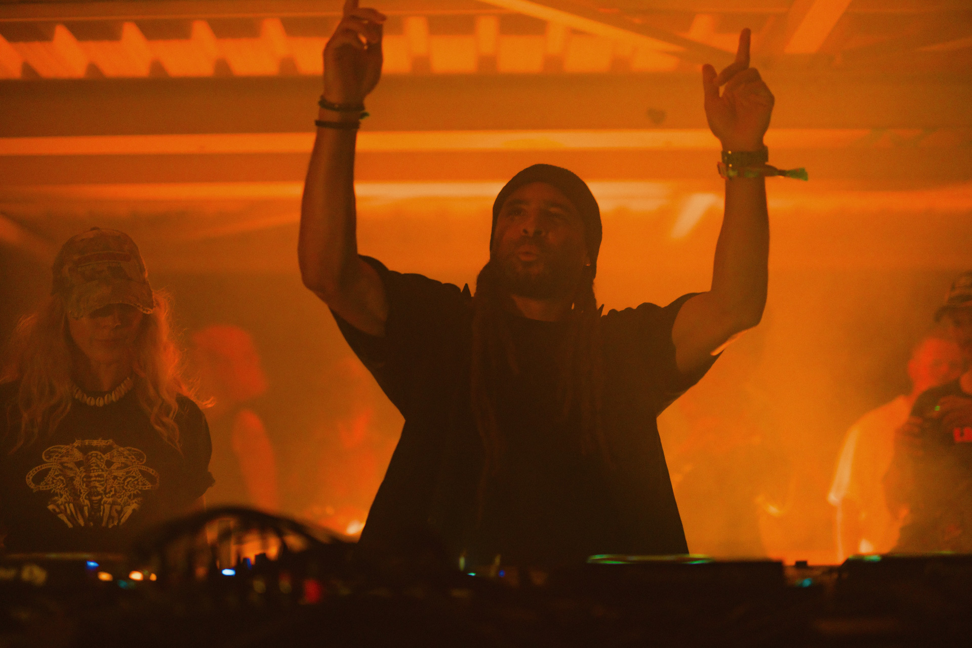 Silhouette of a DJ raising arms in a vibrant orange-lit nightclub.