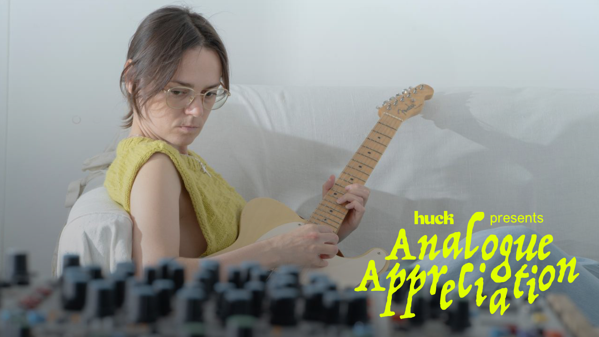 Young woman playing electric guitar on stage with an audience behind her.