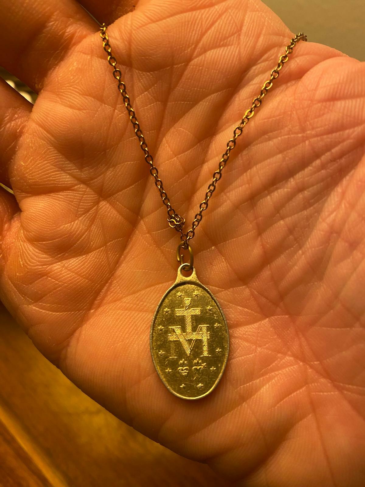 A gold oval-shaped pendant on a gold chain, featuring religious symbols like a cross and the initials 'A.M.'