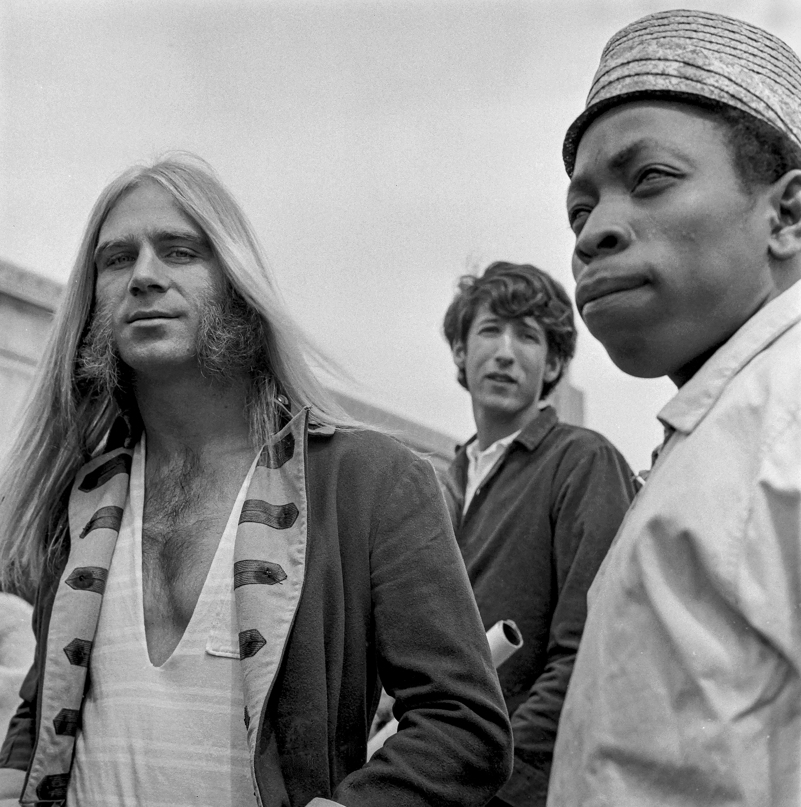 Black and white image of three people, including a woman with long hair and two men, one wearing a hat.