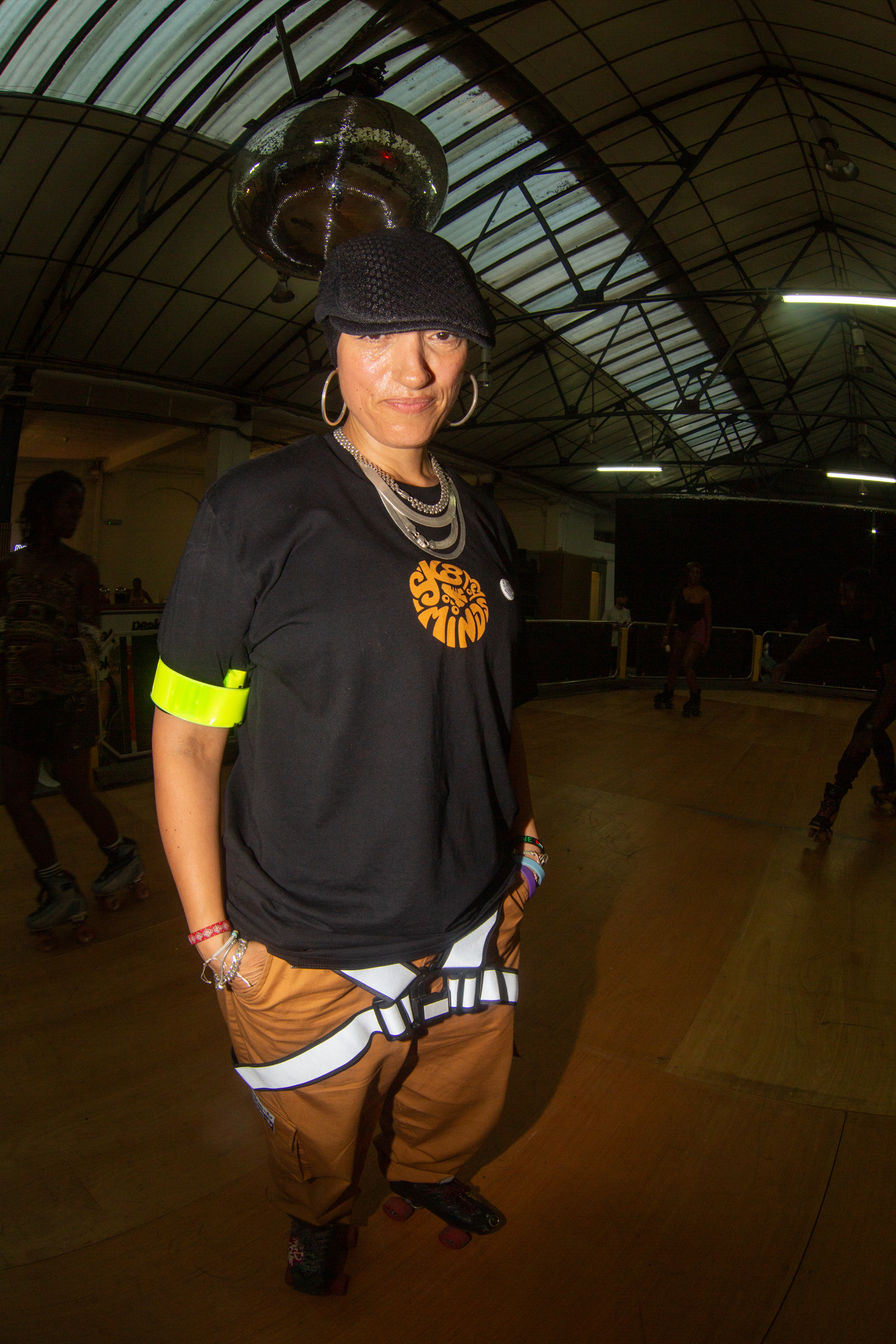 Person in black beanie and oversized black t-shirt with orange graphic stands in warehouse with arched glass ceiling and metal framework.