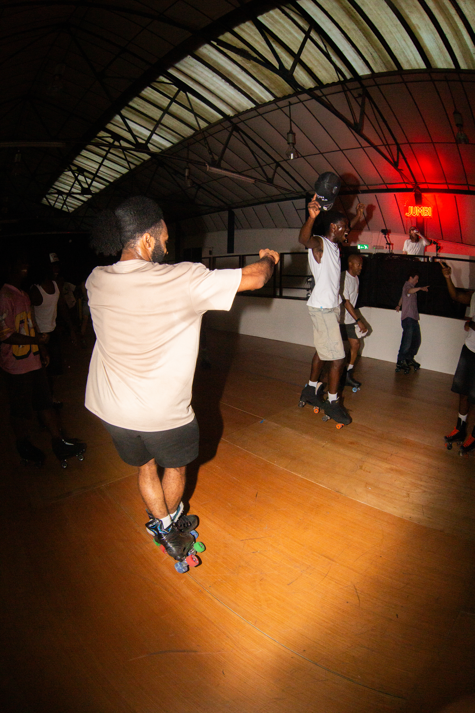 People roller skating in indoor rink with wooden floor, exposed beam ceiling, and red lighting in background.