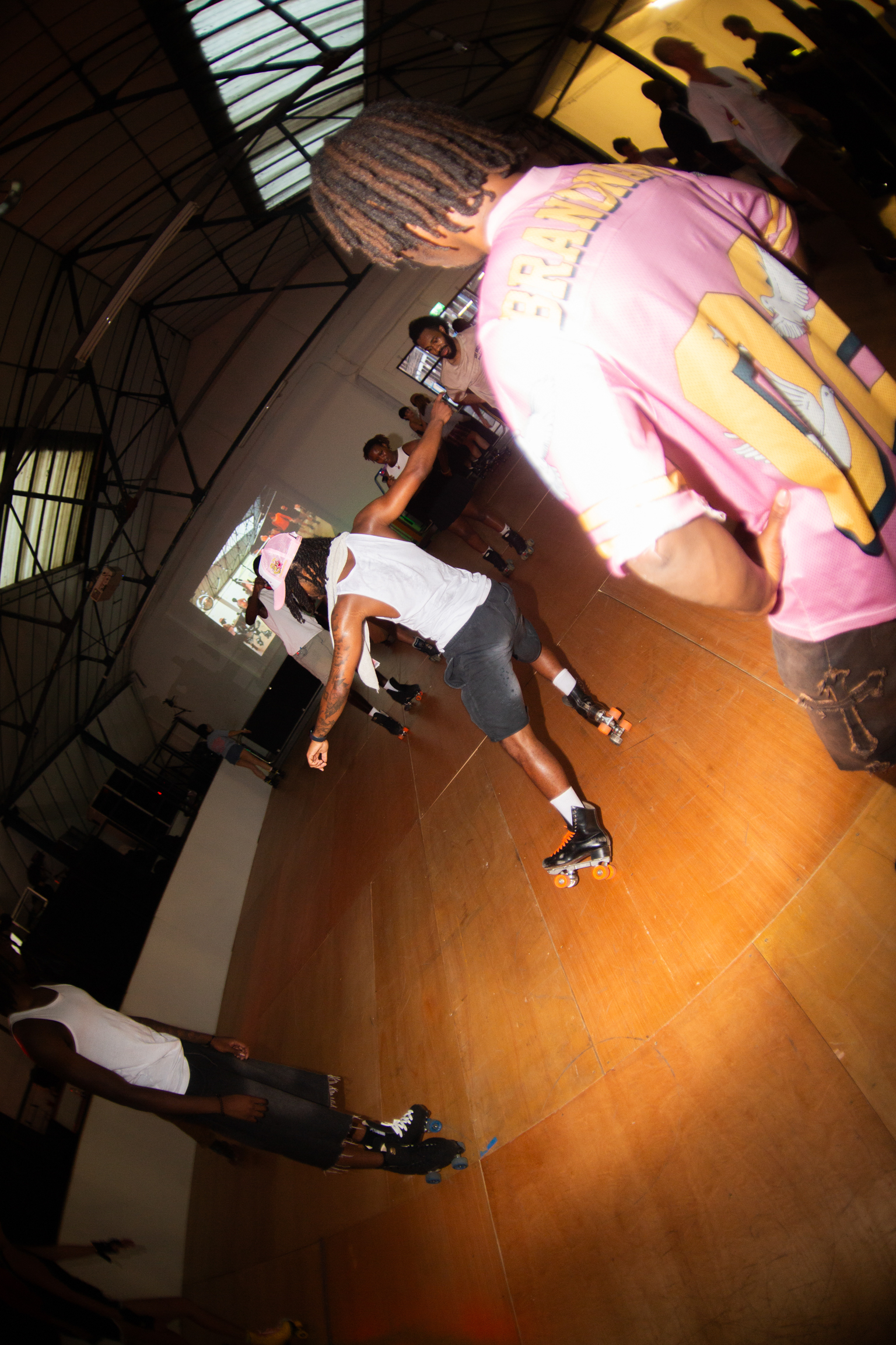 Skateboarder mid-air in bowl with pink and yellow projected visuals on curved walls, industrial ceiling with metal beams visible.