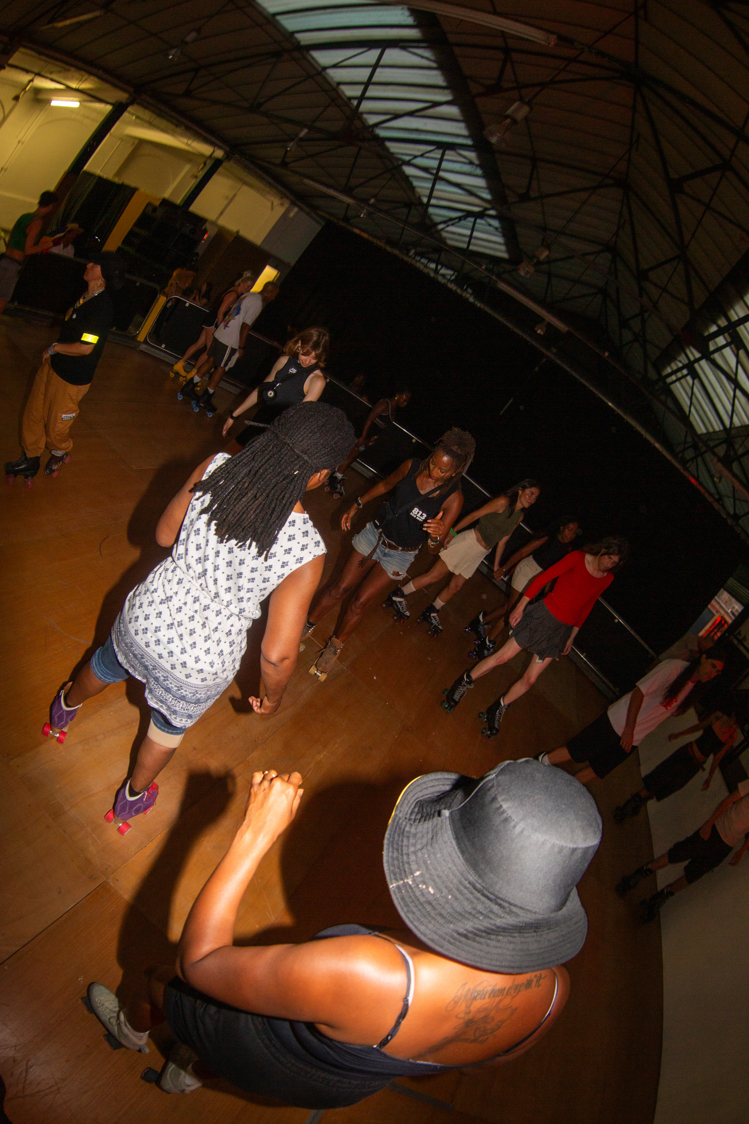 People dancing in crowded indoor venue with glass roof, warm yellow lighting, woman in white top and denim shorts in foreground.