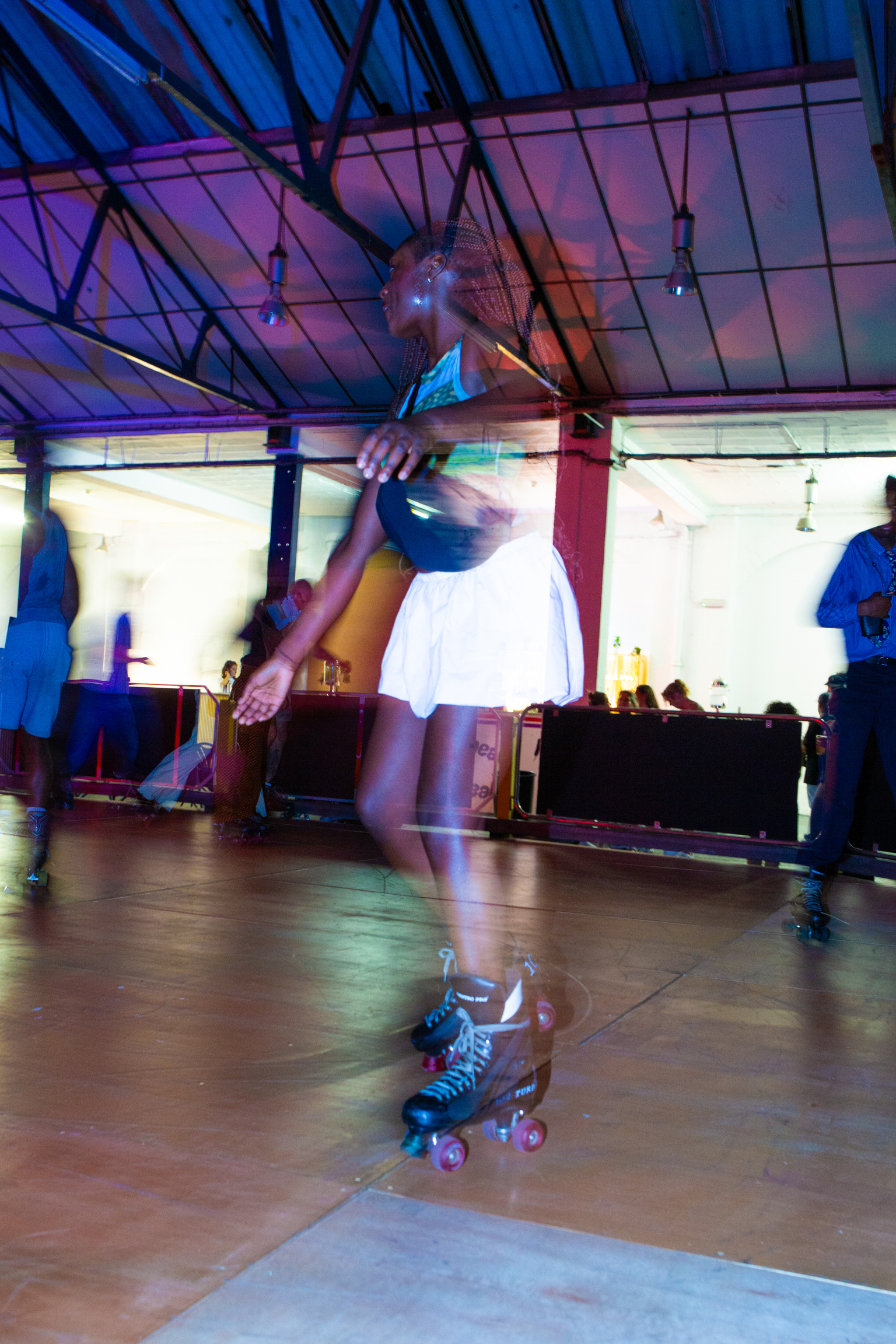 Person roller skating indoors under coloured lighting, creating motion blur effect with purple and blue tones throughout the scene.