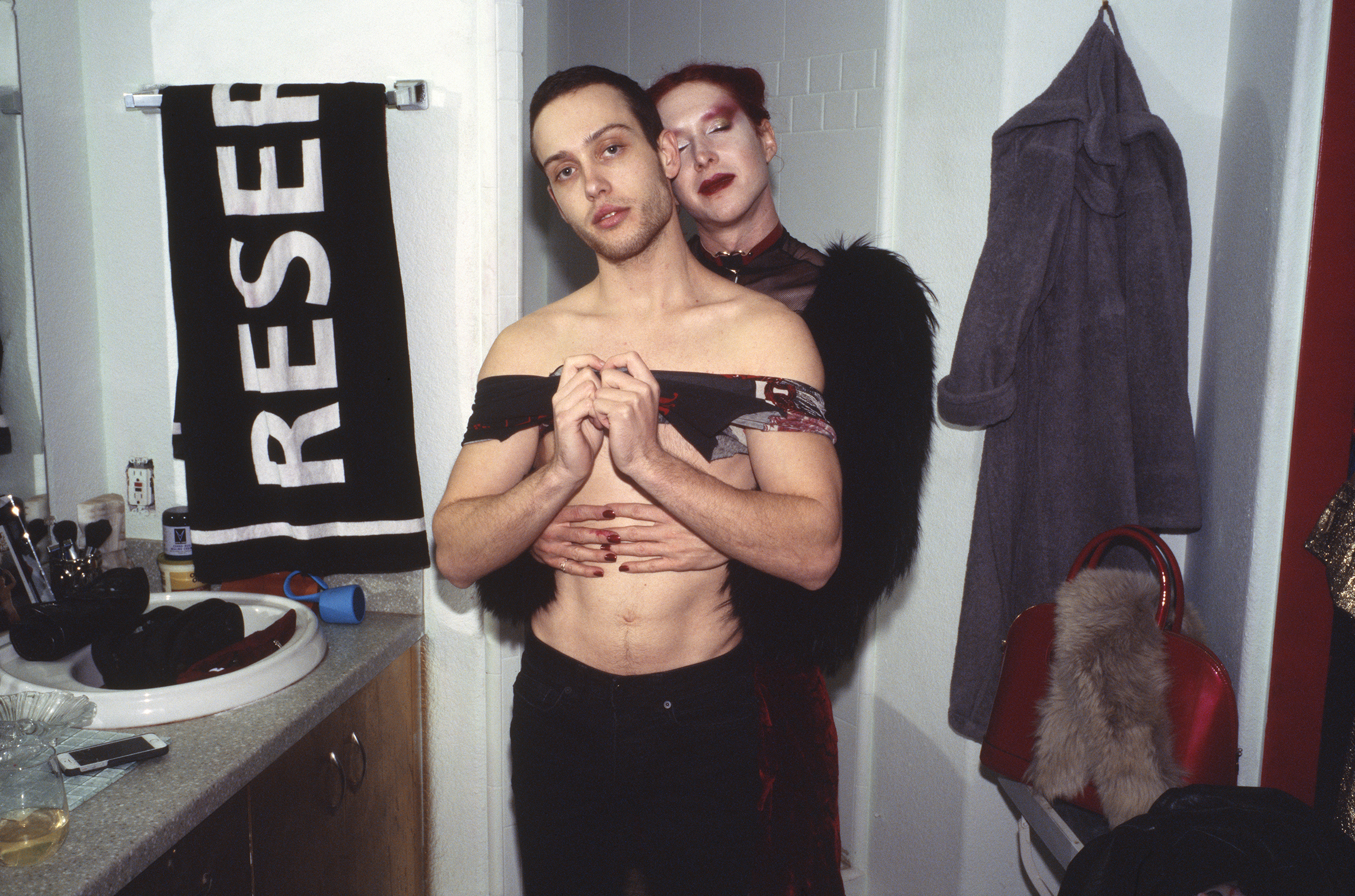 Two shirtless men, one with black hair and the other with red hair, embracing in front of a 'RESET' banner.
