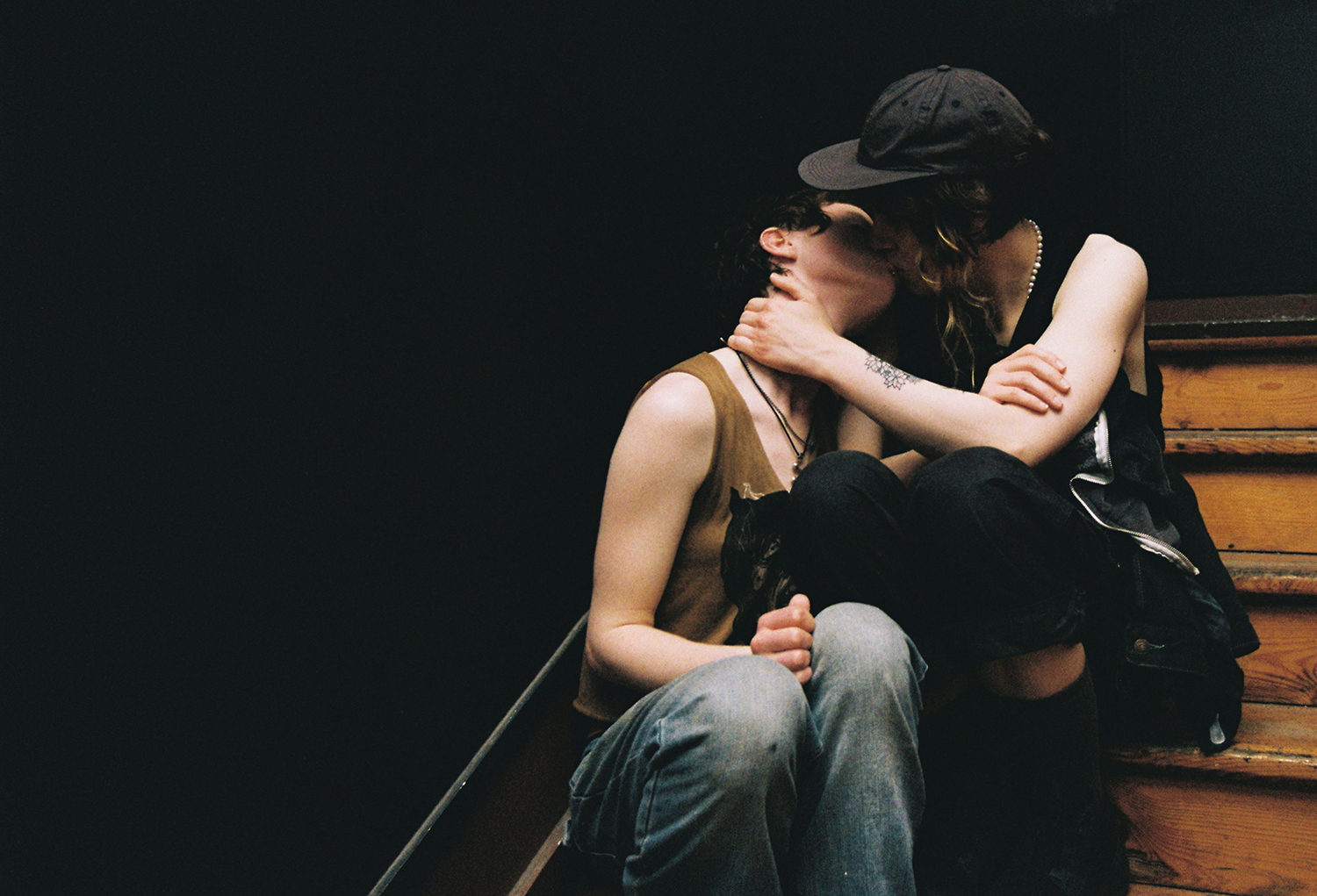 A person huddled on a bench, knees pulled up, arms wrapped around themselves in a protective pose, against a dark background.