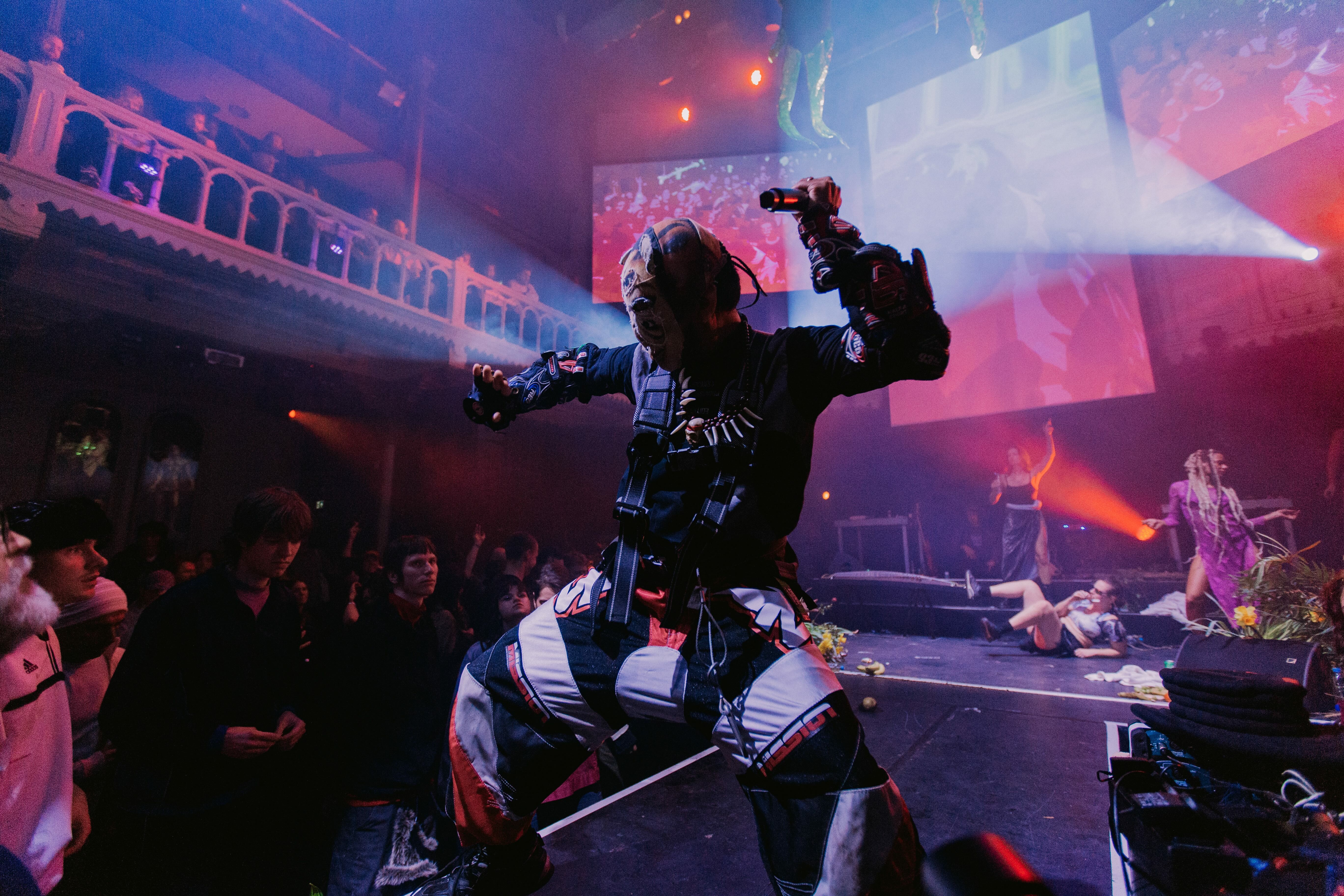 Energetic music performance on stage with colourful lighting, smoke and audience.