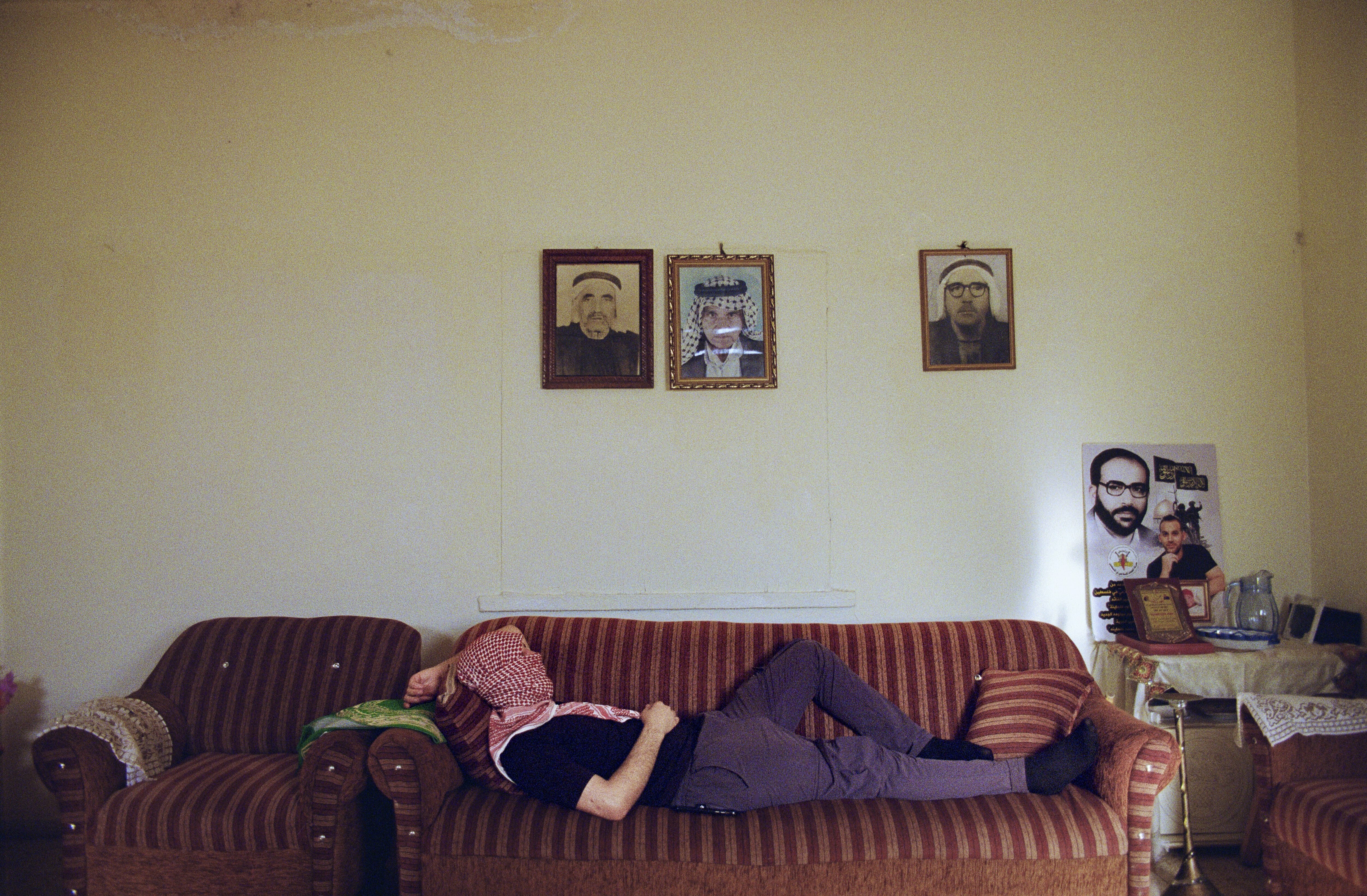 Three framed portraits on a wall above a striped sofa, with a person lying on the sofa.