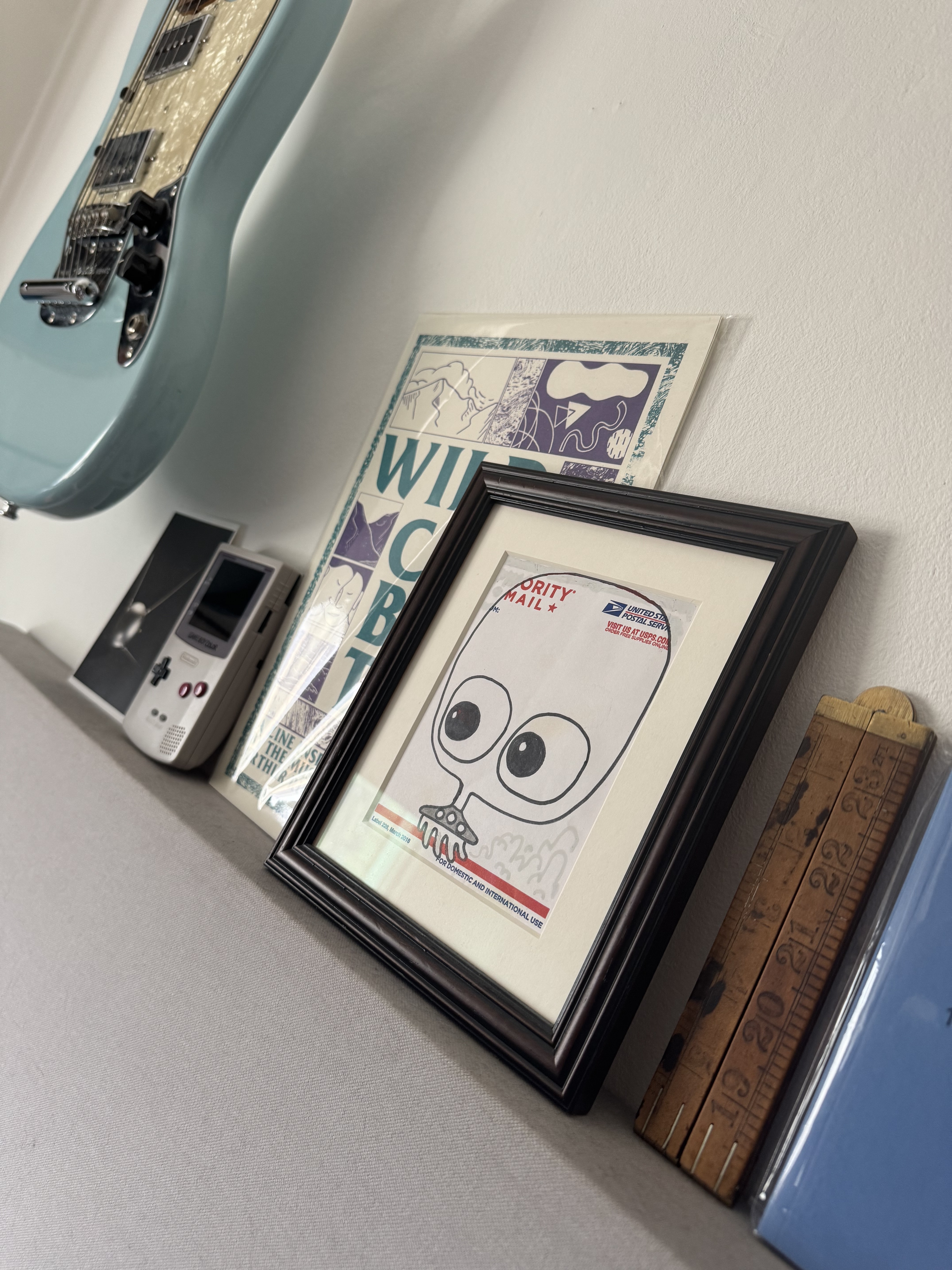 Framed cartoon drawing of a character with large eyes and open mouth on a wall, surrounded by various other items such as a record player and other wall art.