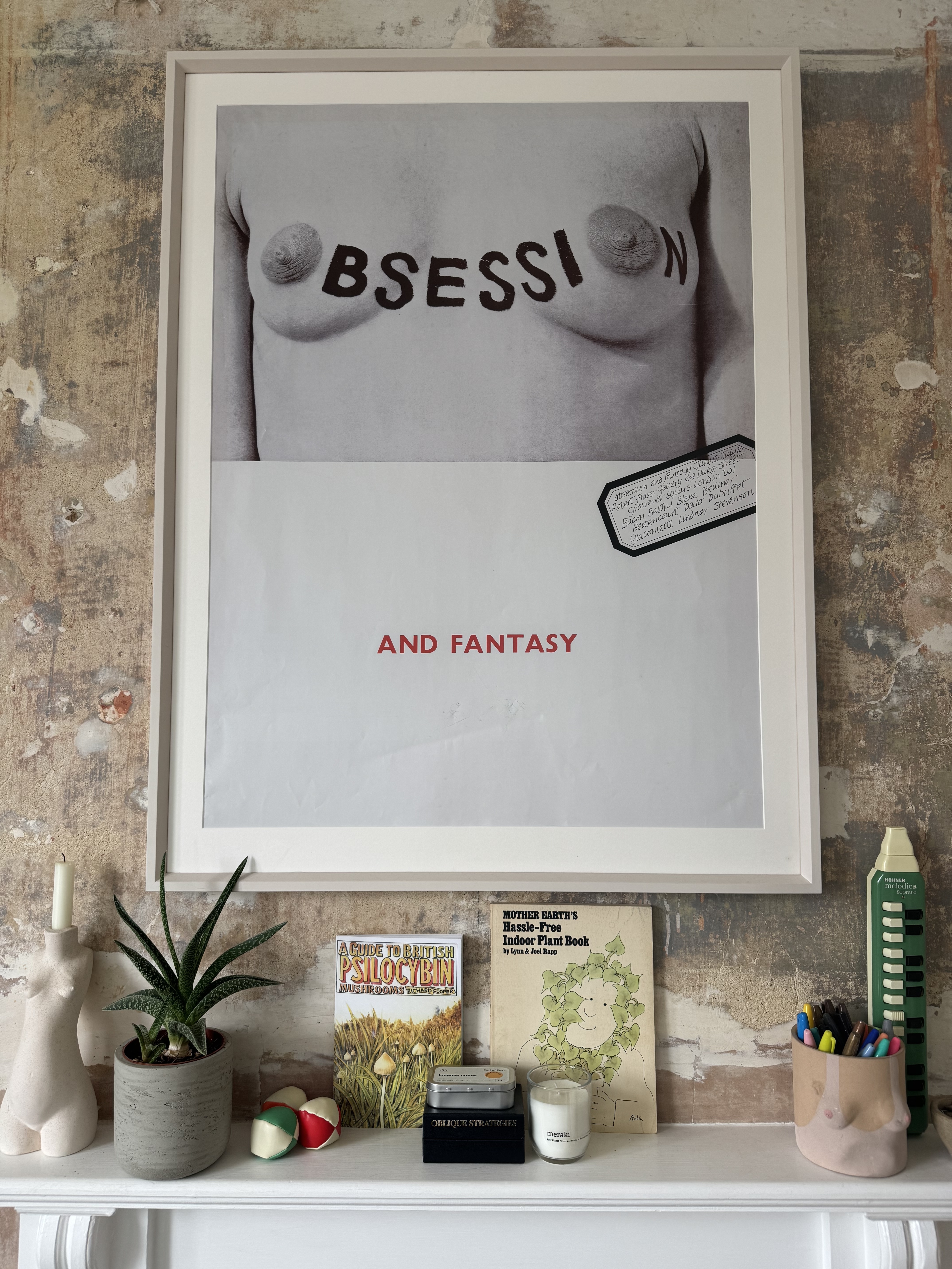 Framed image featuring the text "BSESSI" and "AND FANTASY" on a monochrome background. Desk with various objects including plants, books, and a rubber stamp.