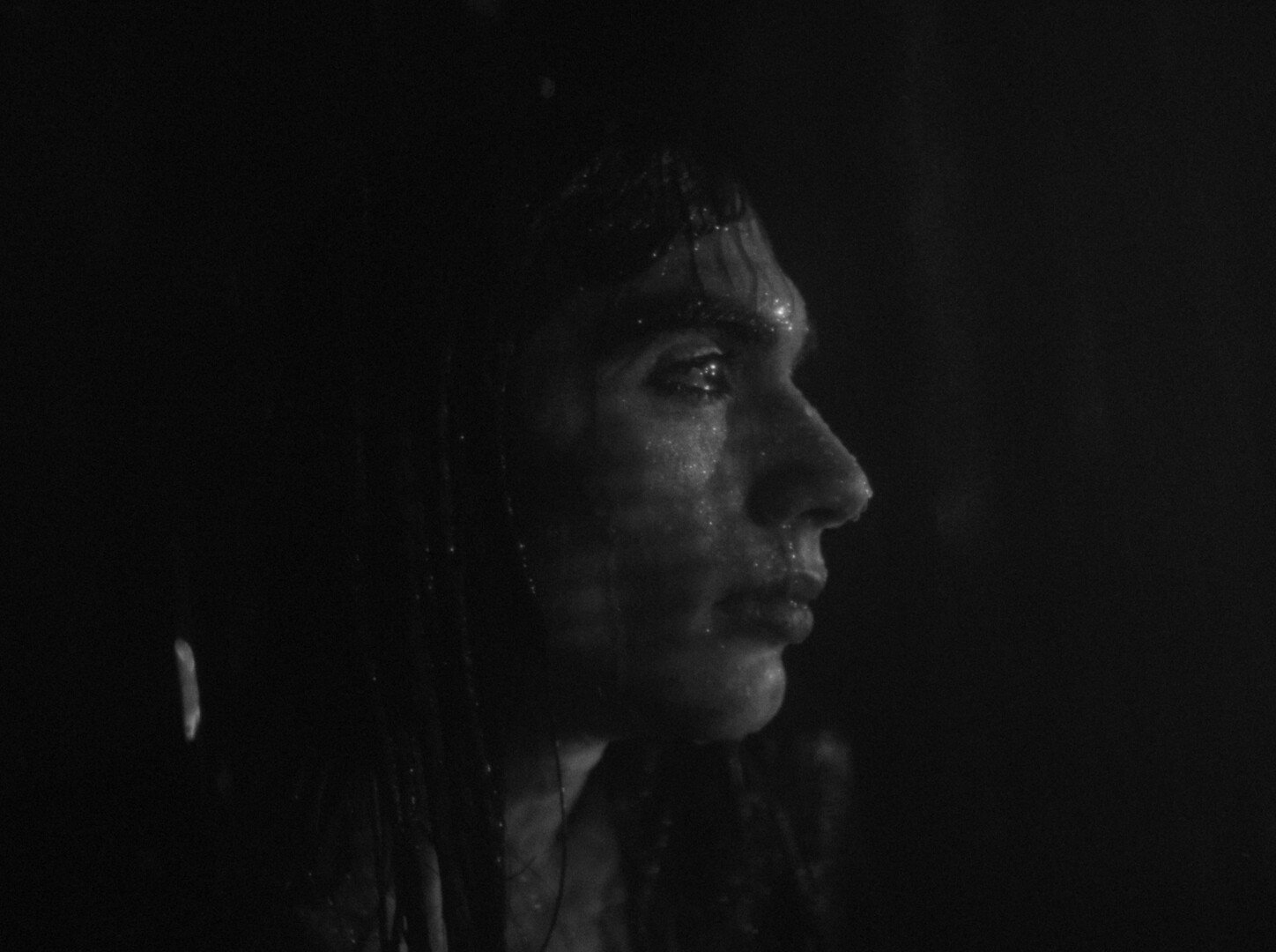 Black and white portrait of person in profile facing right, dramatic lighting highlighting facial features against dark background.