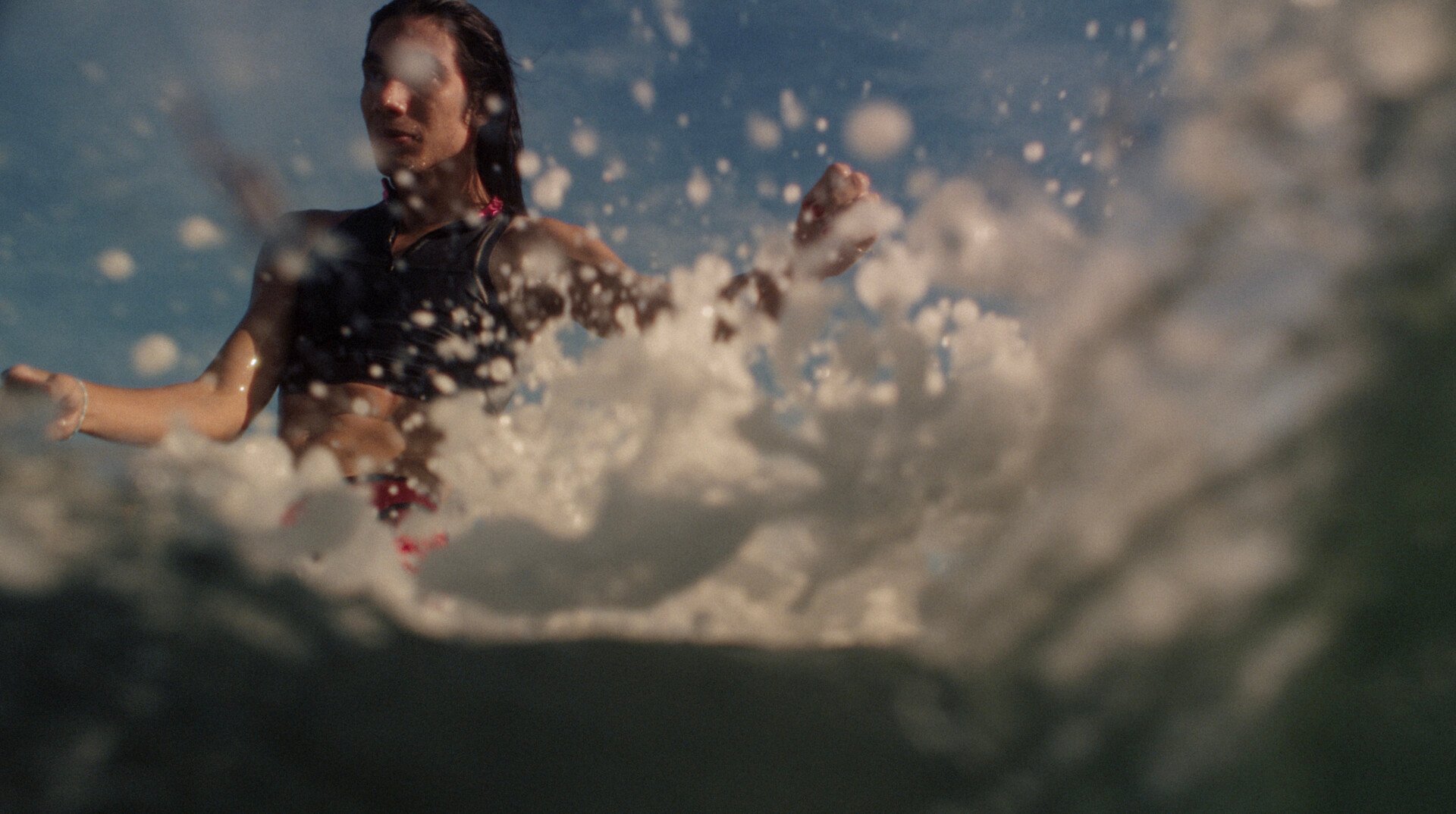 Person swimming in water with large splash creating white foam and droplets around them, mountains visible in blurred background.