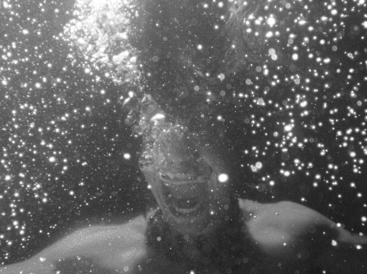 Black and white underwater view showing person submerged with numerous white bubbles scattered throughout dark water around them.