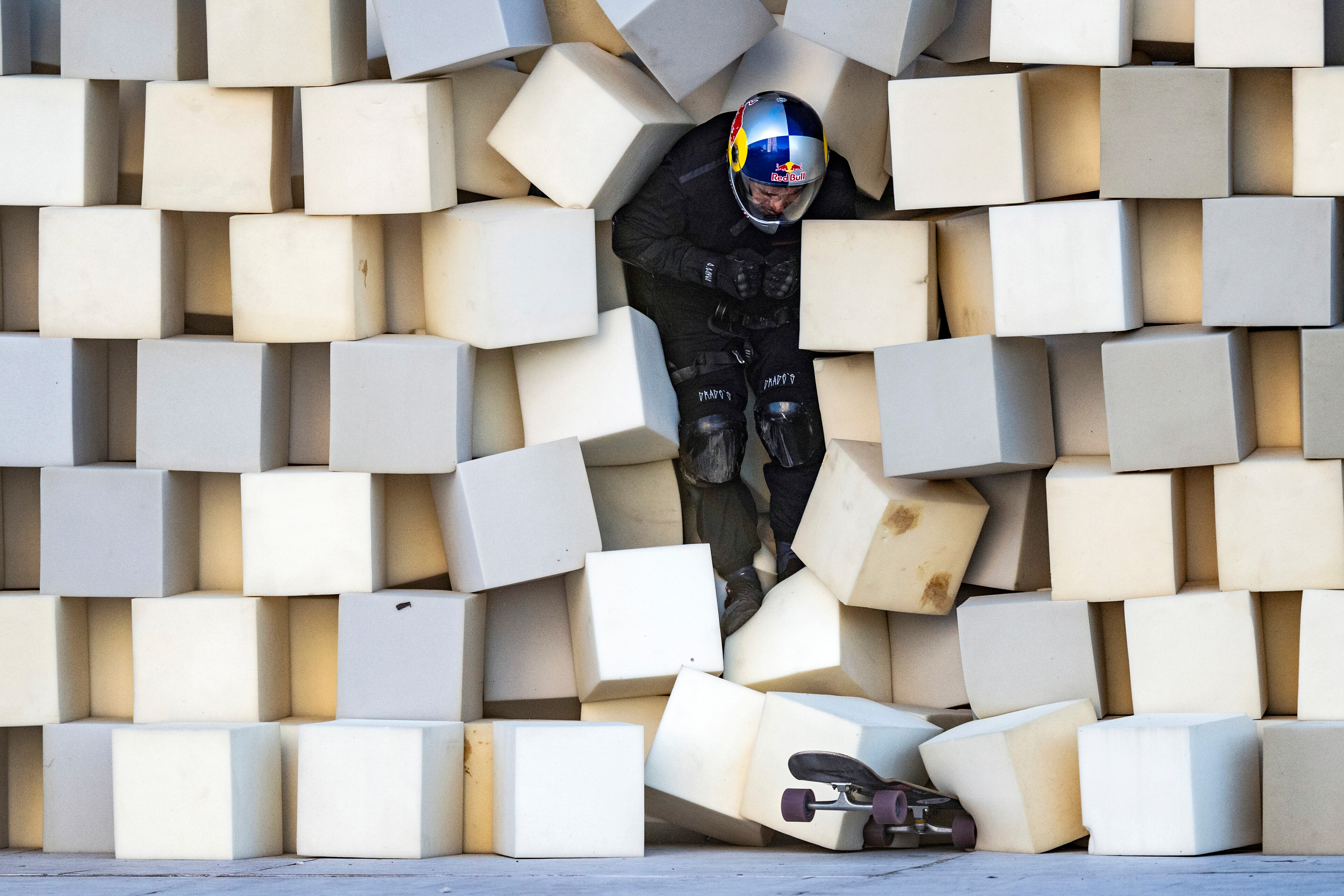 Person in black tactical gear and helmet breaking through wall of white cubic blocks arranged in grid pattern.