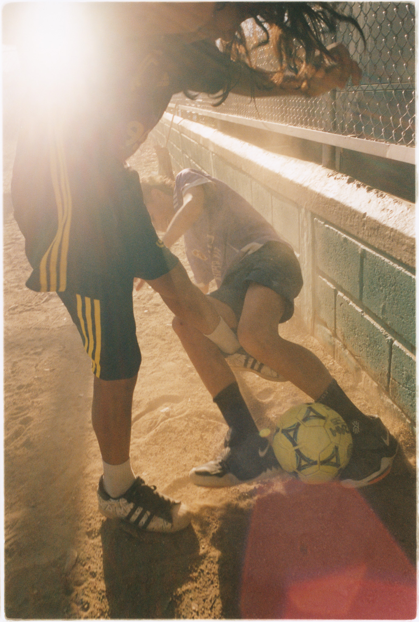A person kneeling on the ground, wearing athletic clothing and shoes, with a soccer ball and other sports equipment nearby.