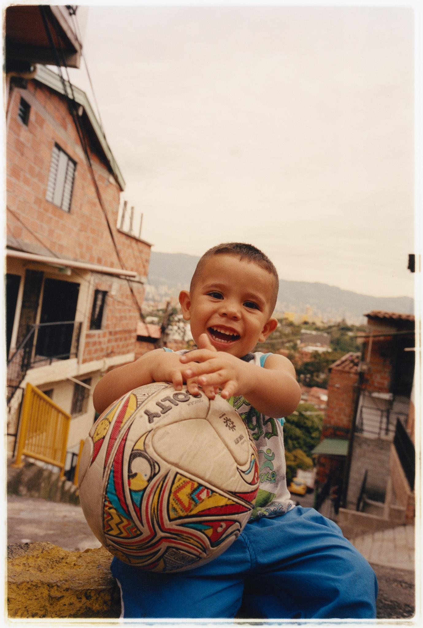 Smiling child holding a decorated football, standing in front of a brick building.