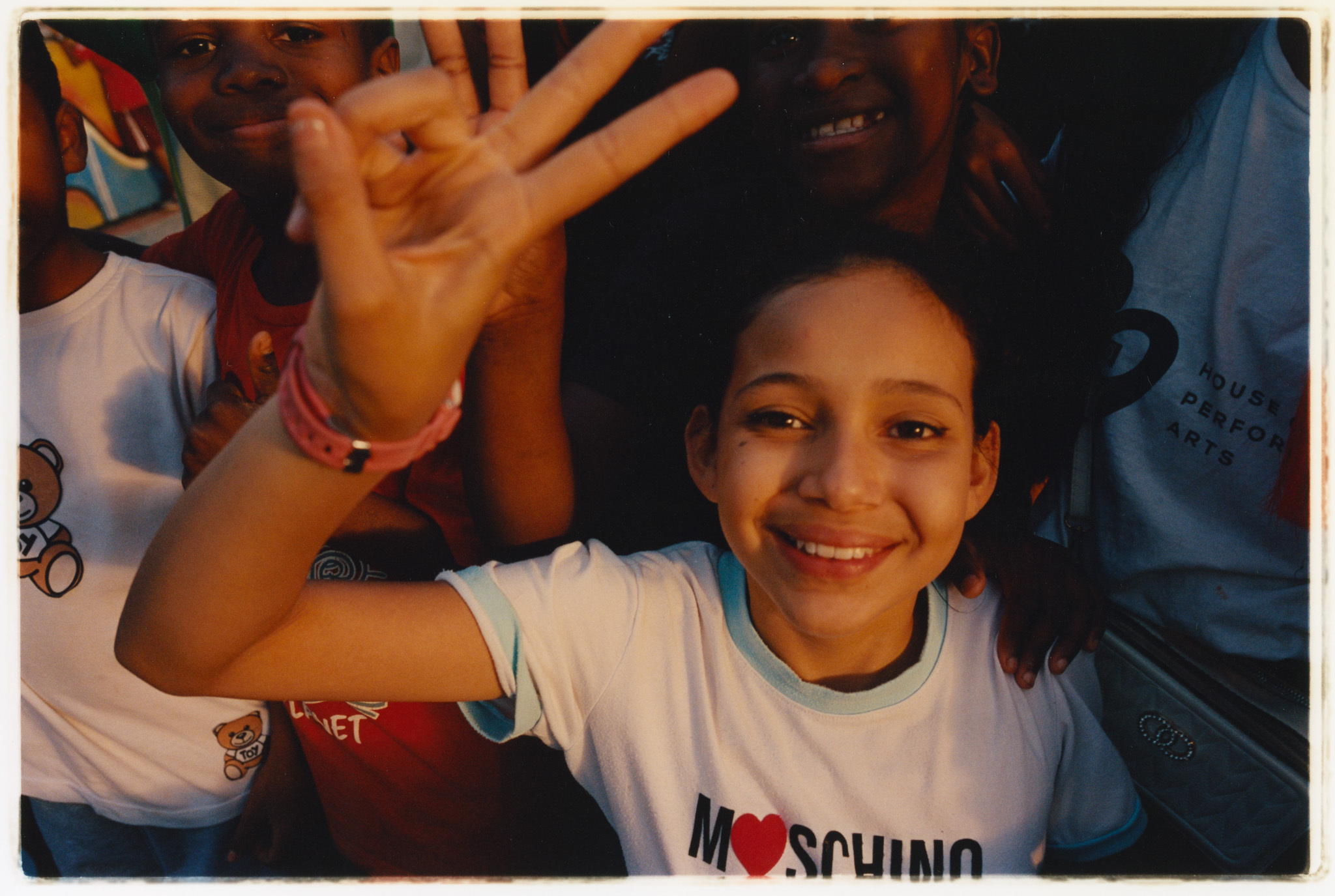 A smiling young person wearing a white t-shirt with a printed logo, gesturing with their hands.