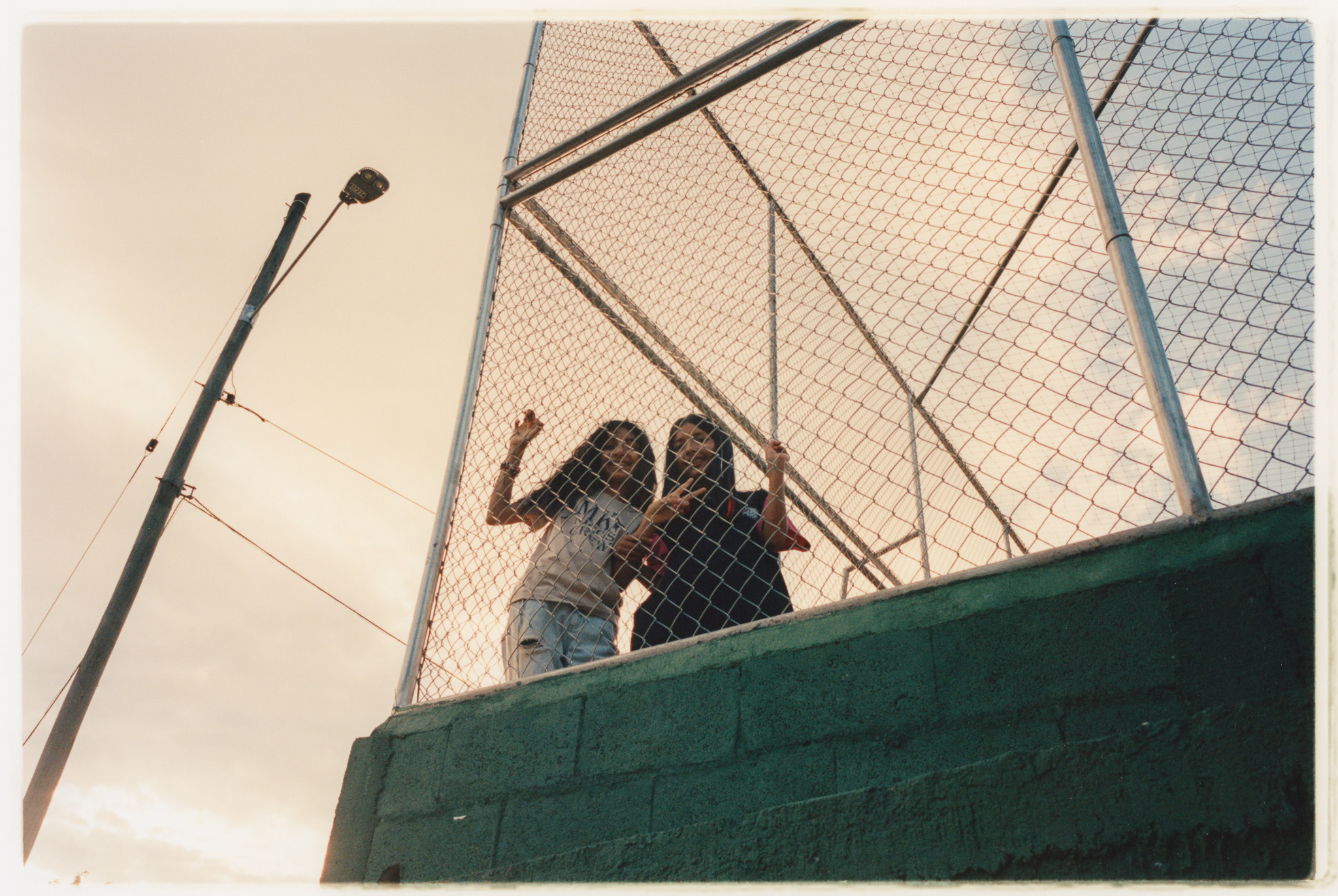 Two silhouetted figures behind a wire mesh fence.