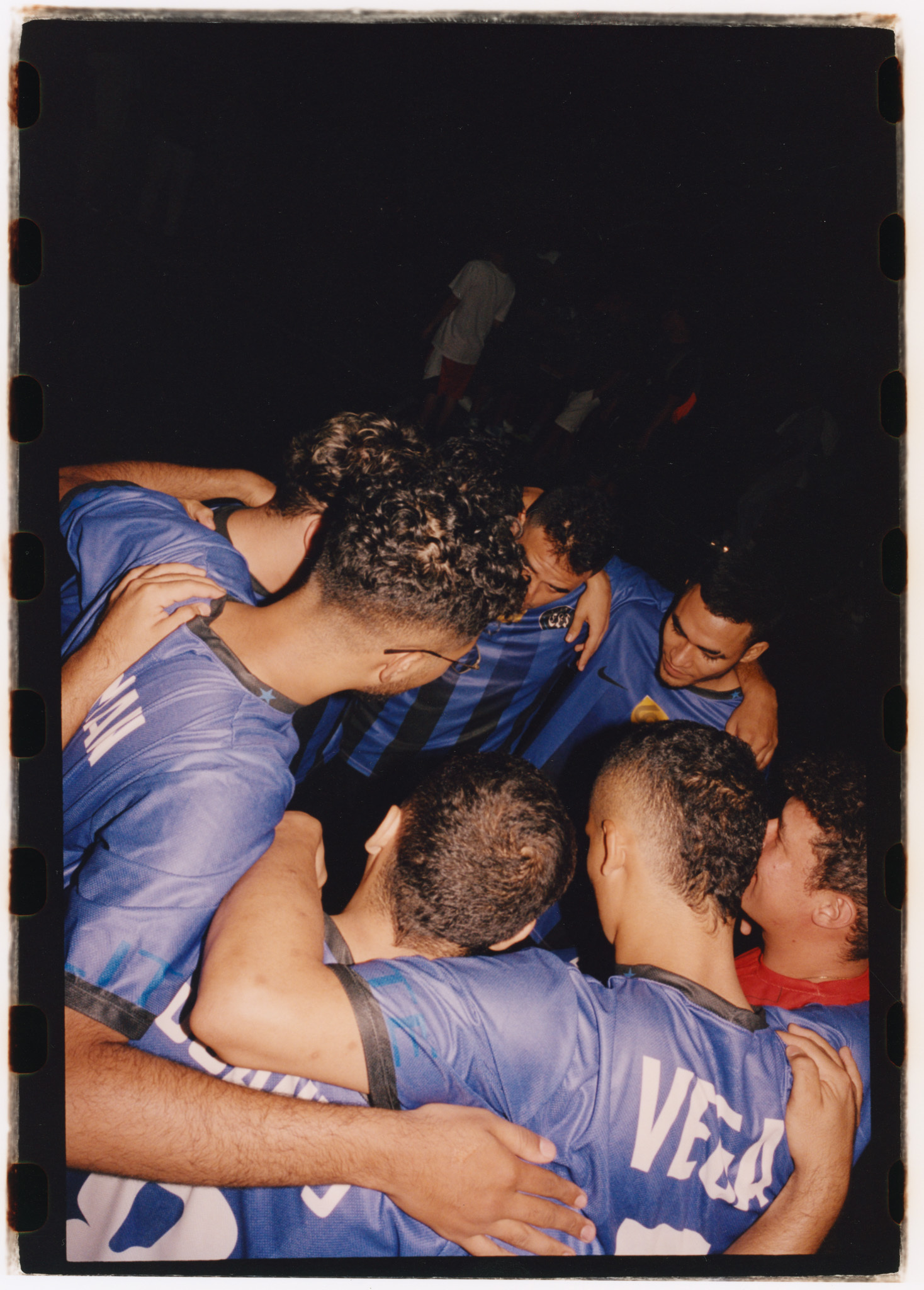Group of young people in sports jerseys hugging and embracing each other in a close group.