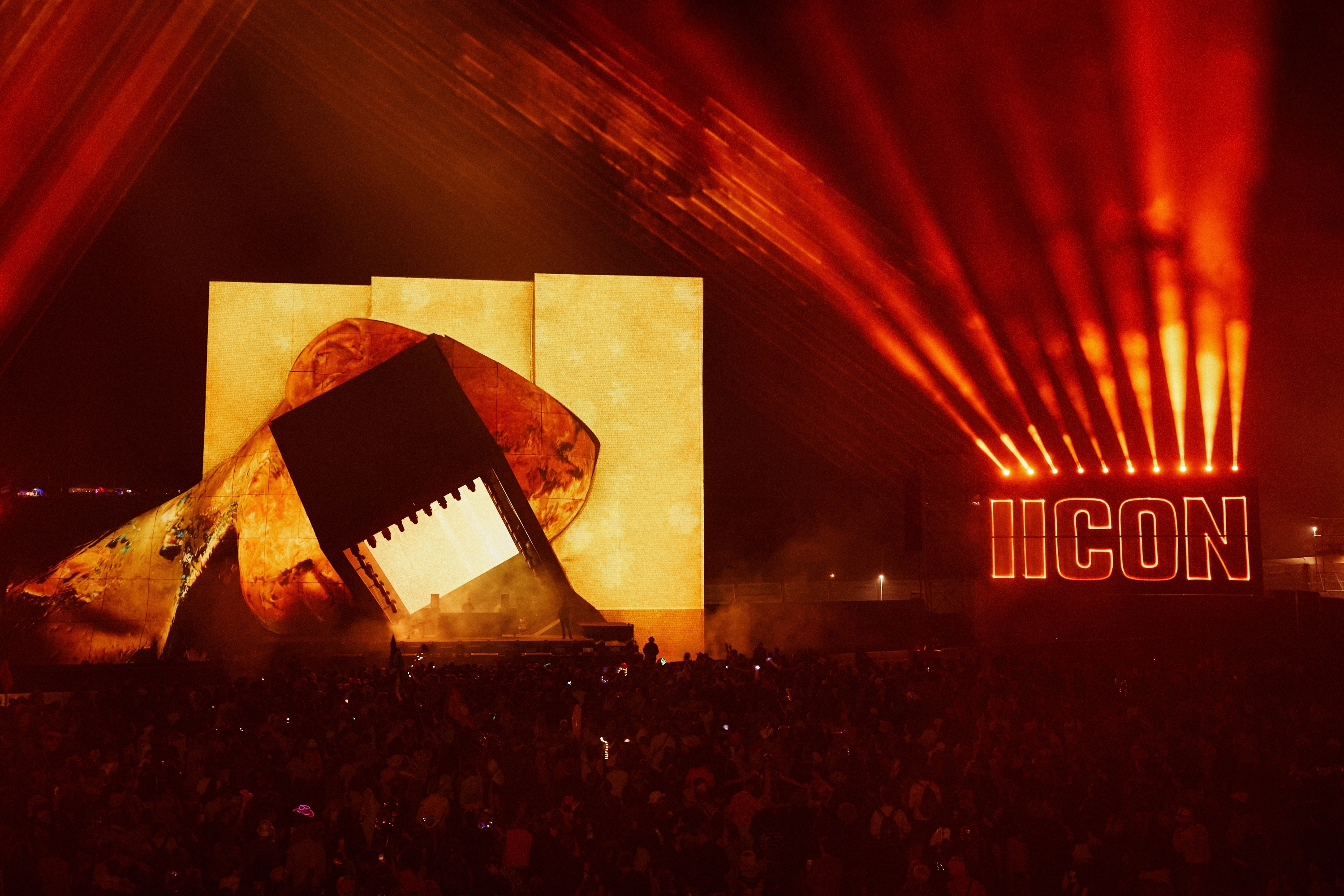 Giant black silhouette of person on stage, backlit by orange and red lights, with "ICON" sign in the background.