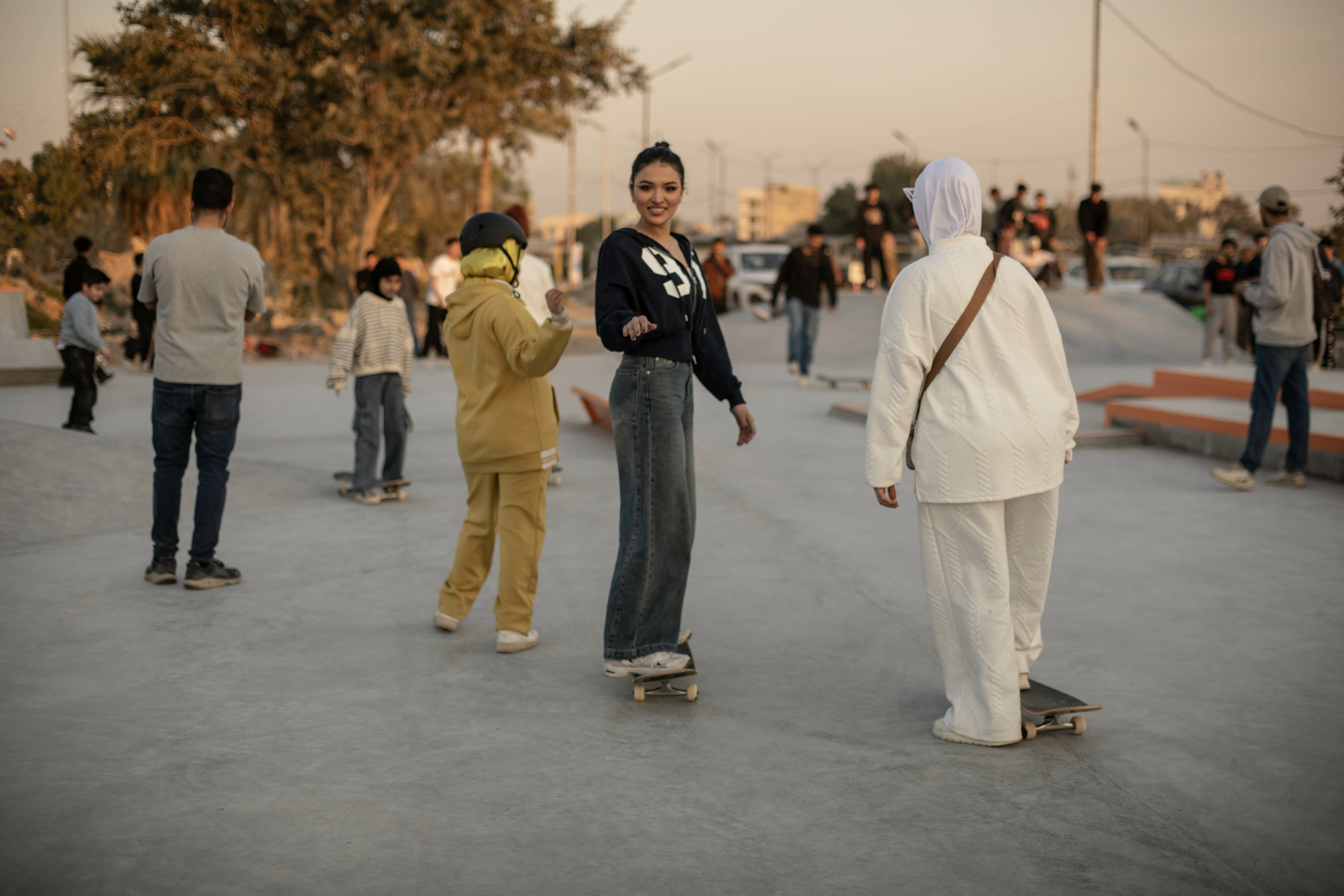 A group of people skateboarding and socialising in a public space, with a sunset backdrop.