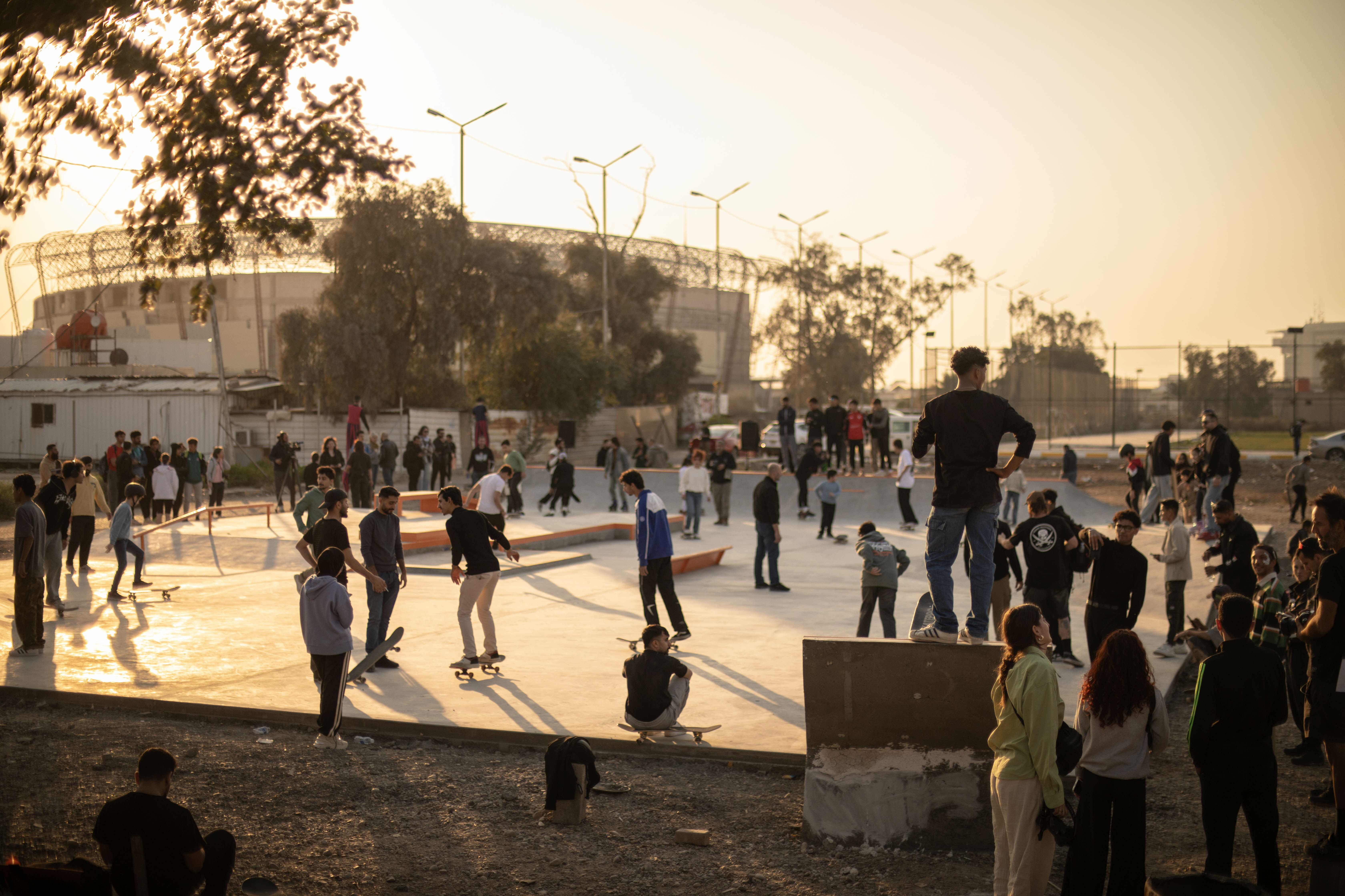 Busy outdoor ice skating rink with people of various ages enjoying the activity, surrounded by trees and buildings in the background.