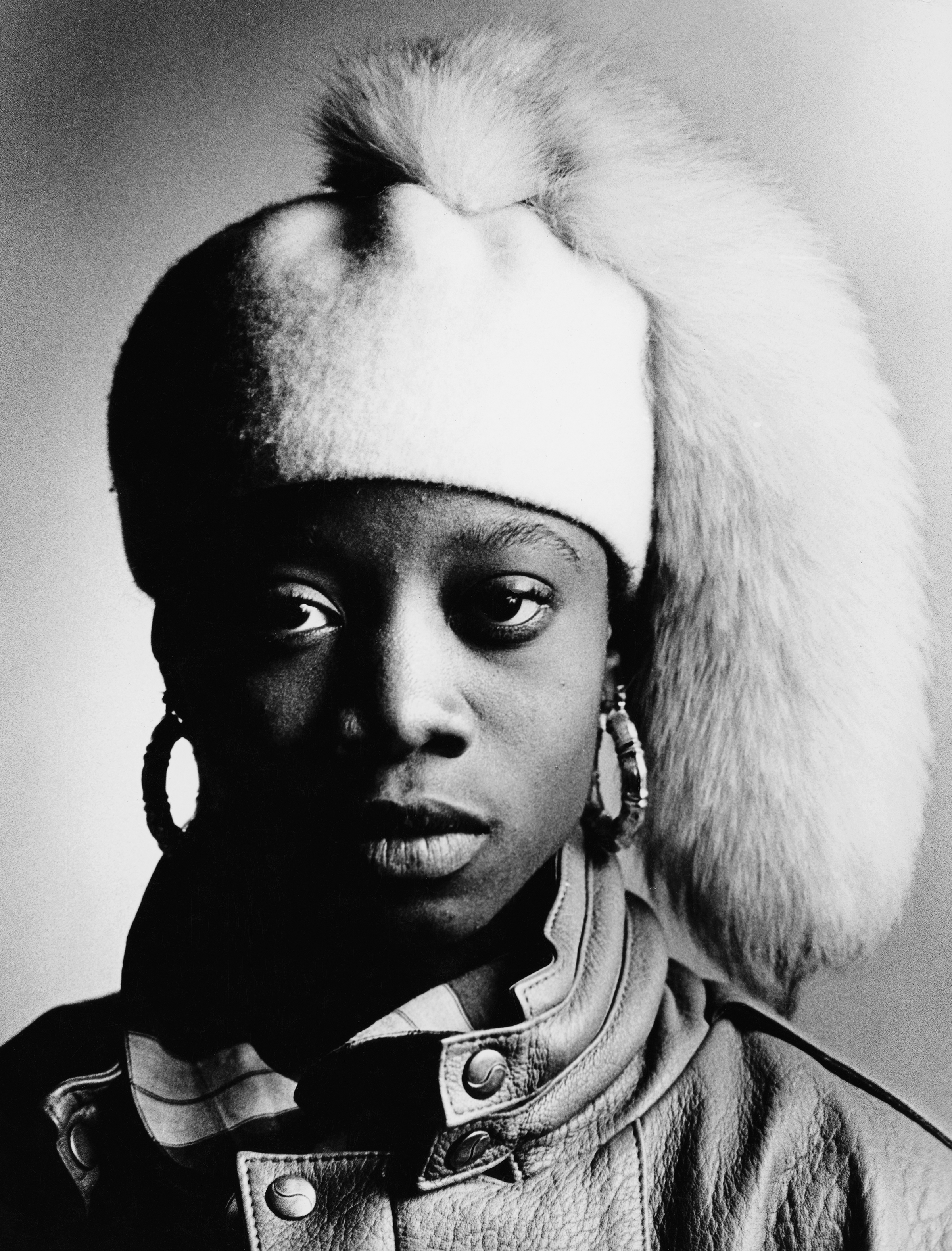 Black and white portrait of person with blonde mohawk hairstyle, large hoop earrings, and leather jacket with metal studs.