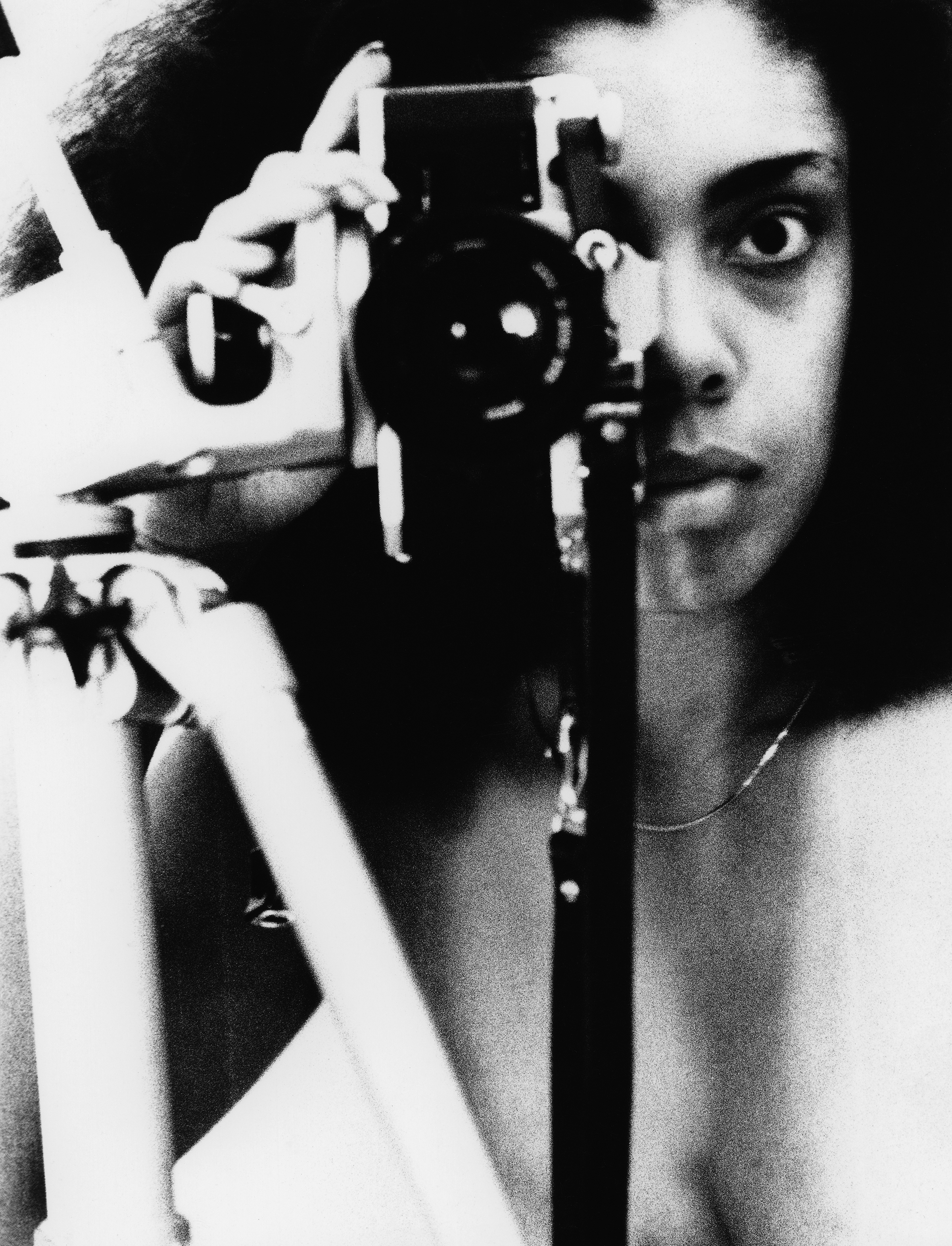 Black and white image of woman holding vintage camera to her face, one eye visible beside lens, dramatic lighting and shadows.