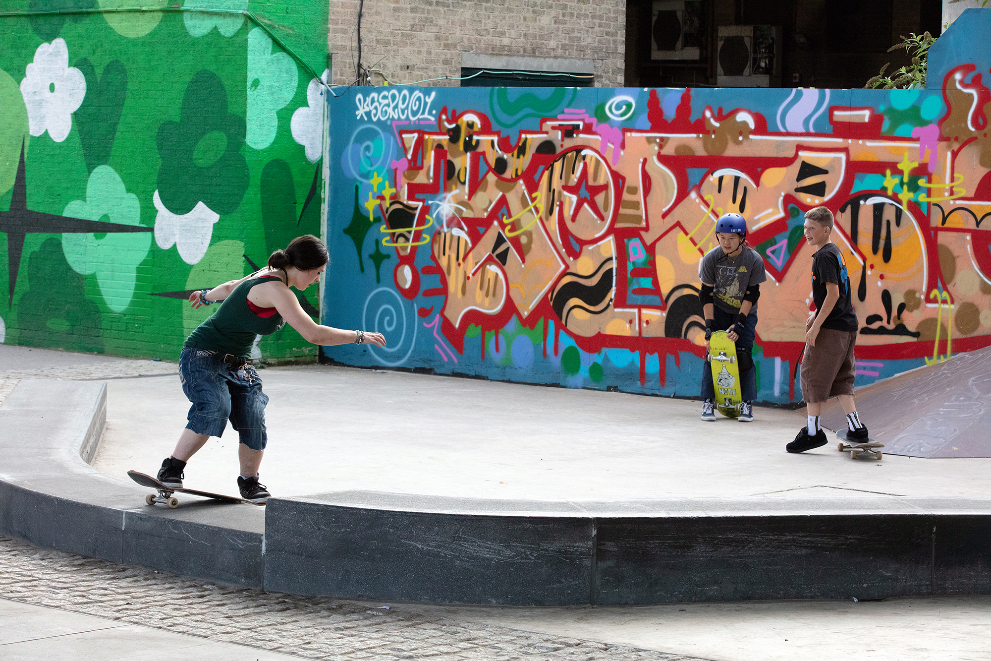Skateboarder in motion at concrete skate park with colourful graffiti wall featuring green, blue, red, and yellow street art.