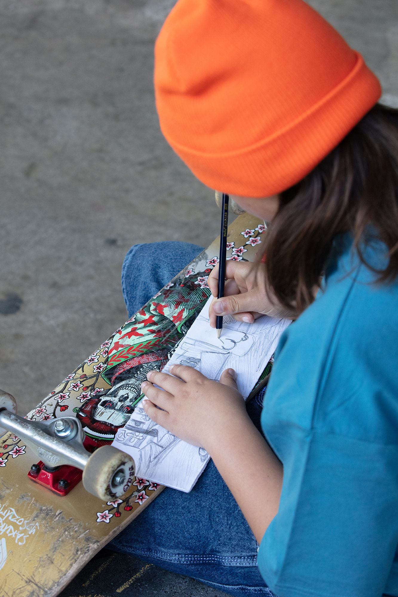 Person in orange beanie and blue top working on jigsaw puzzle, seated at table with colourful skateboard nearby.
