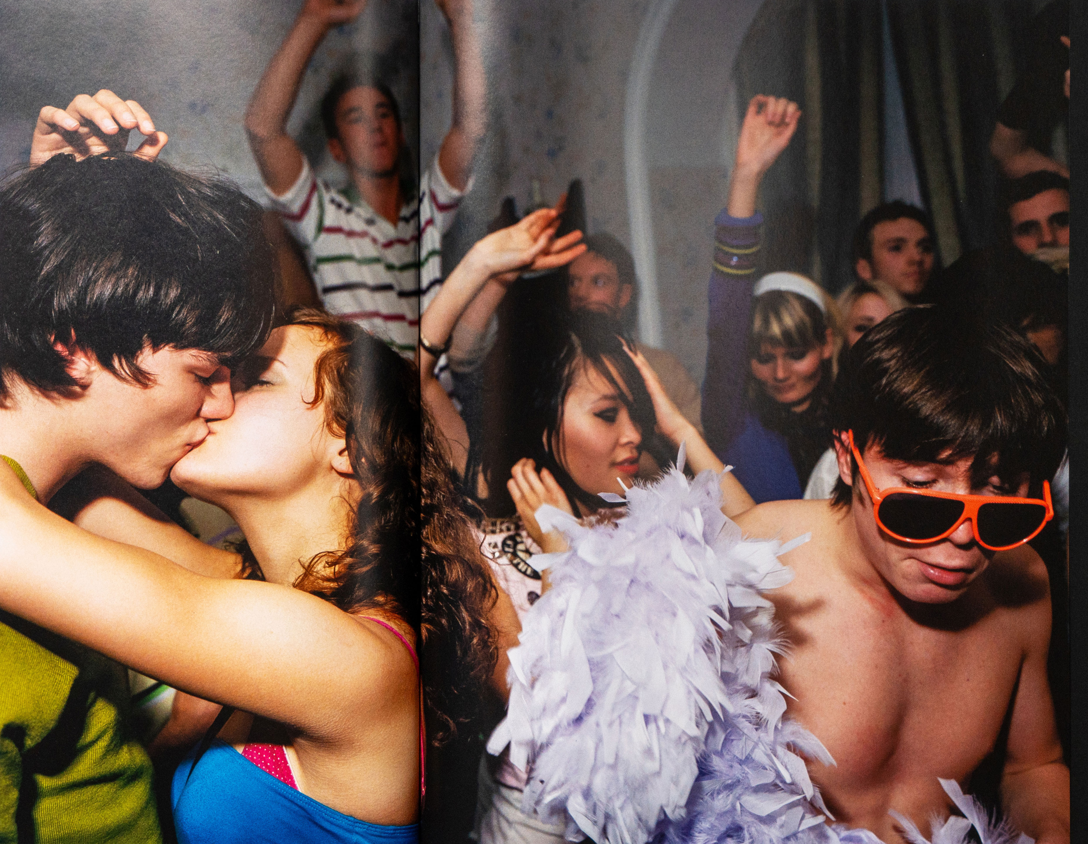 Group of young people dancing and embracing at a nightclub, with neon lighting and colourful outfits.