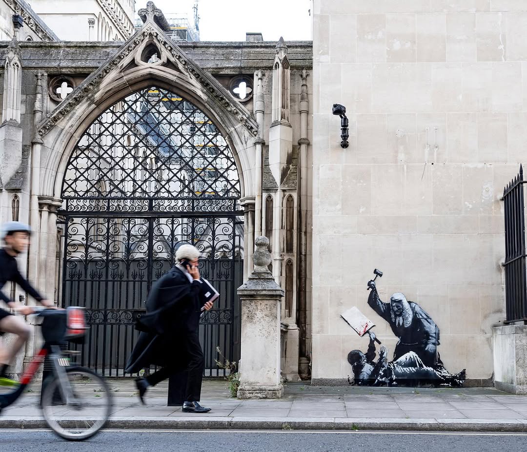 Gothic stone archway with ornate metalwork beside modern street art depicting figures with umbrellas on weathered wall.