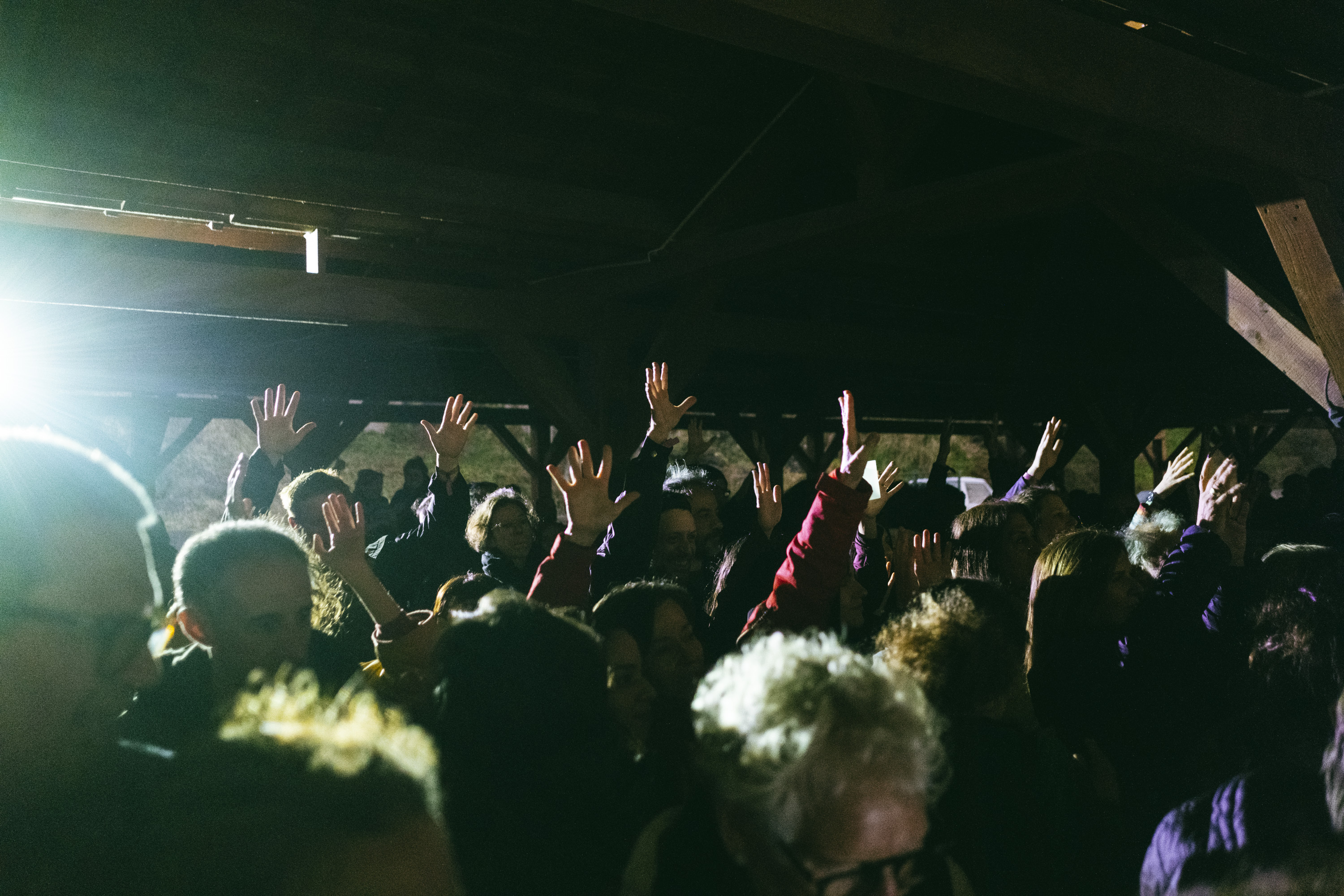 Crowd of people with hands raised, silhouetted against bright stage lights in a dark setting.