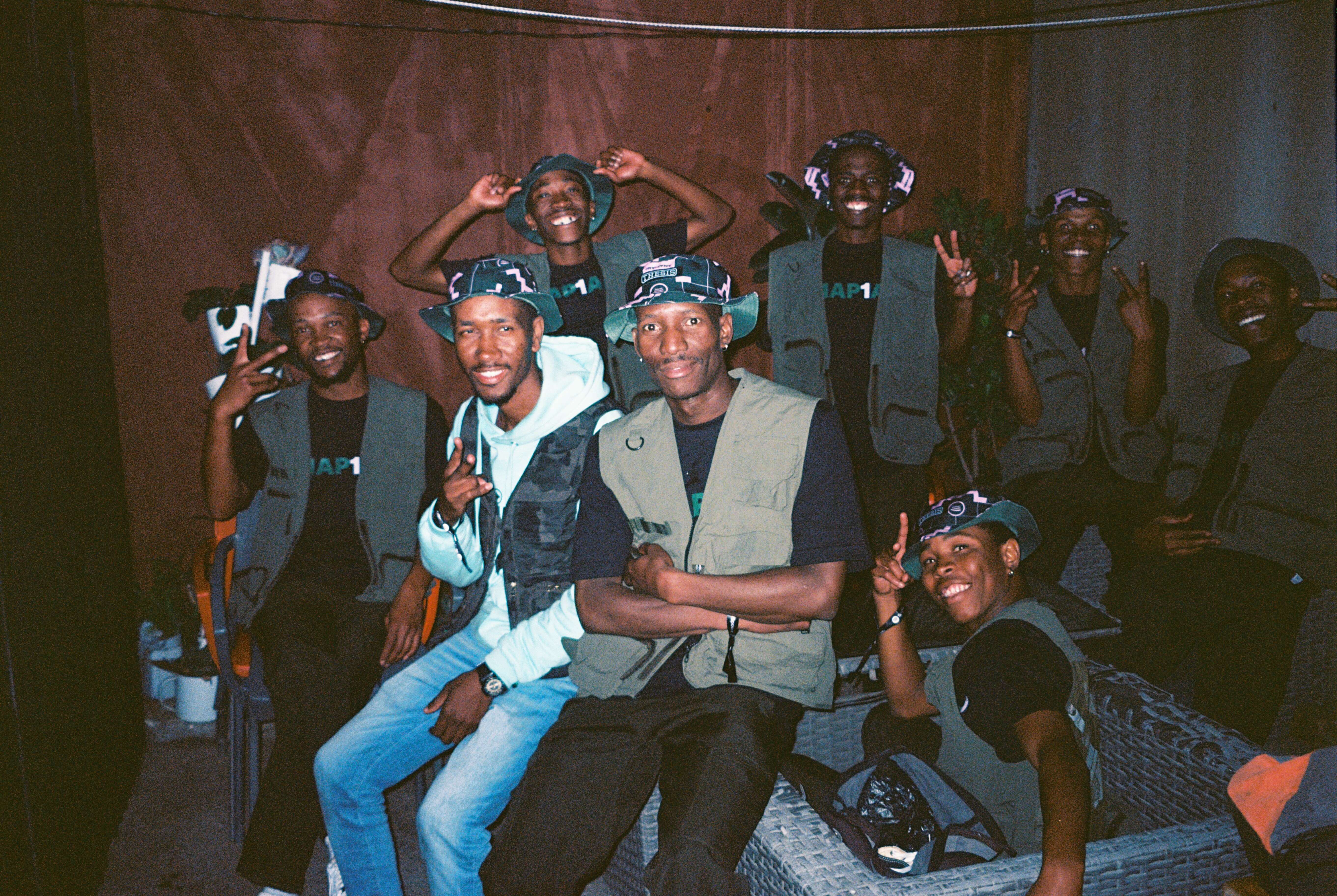 Diverse group of people in casual clothes, gesturing and smiling, in a dimly lit indoor setting.