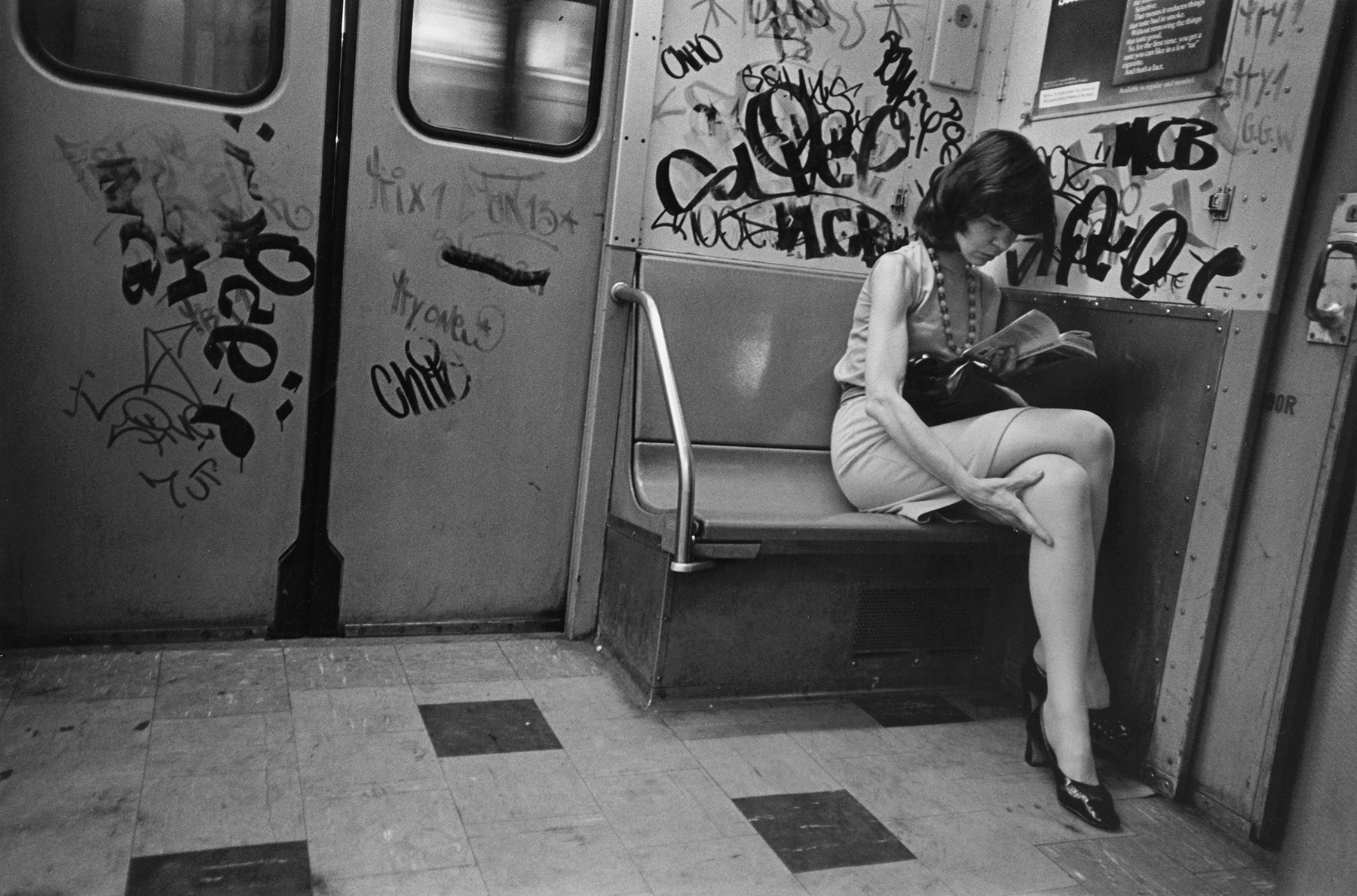 A person sitting alone on a bench in a graffiti-covered subway carriage.
