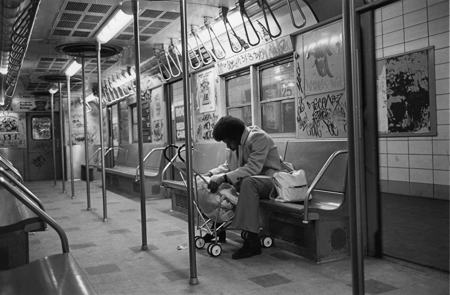 Black and white image of subway carriage interior with sleeping man seated on bench