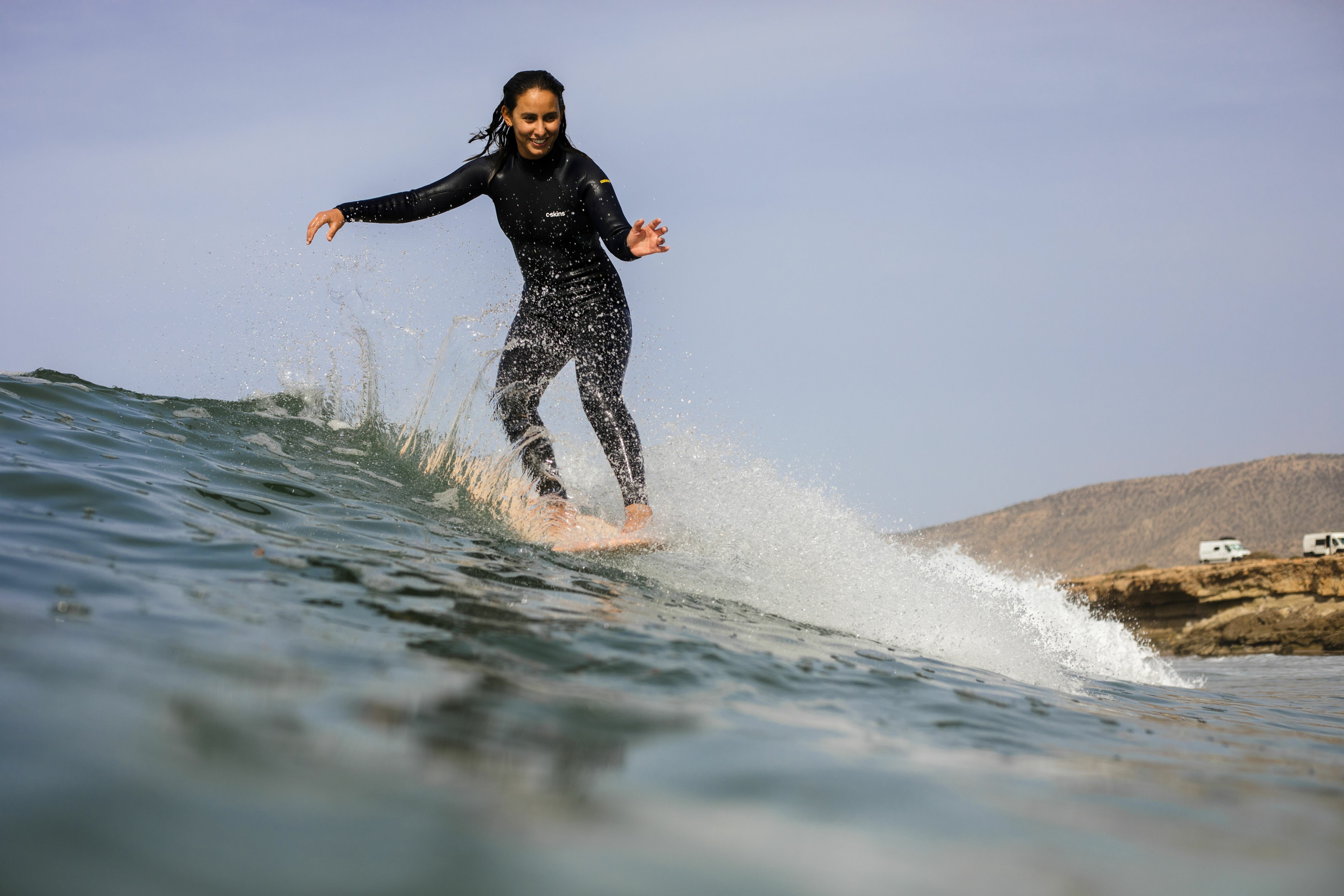 A person in a wetsuit surfing a wave in the ocean, with rocky cliffs in the background.