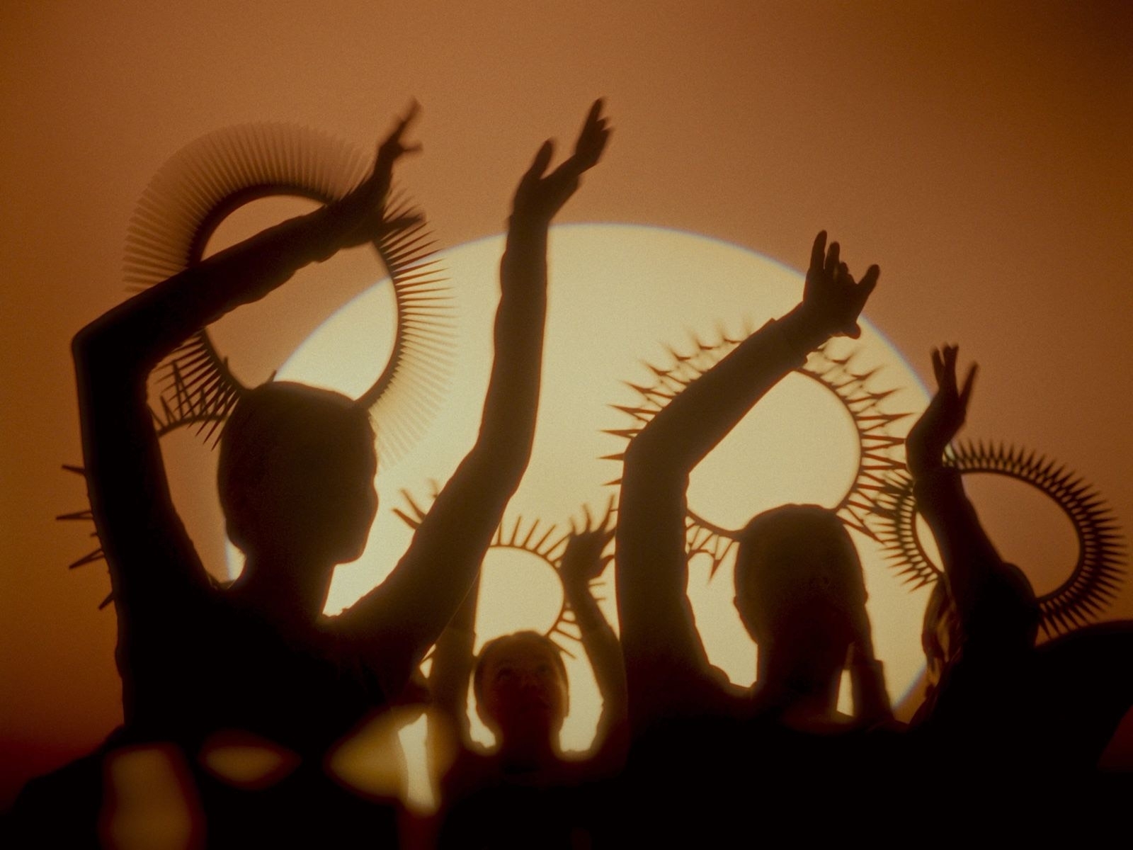 Silhouettes of dancers against an orange backdrop, with arm motions conveying movement and energy.