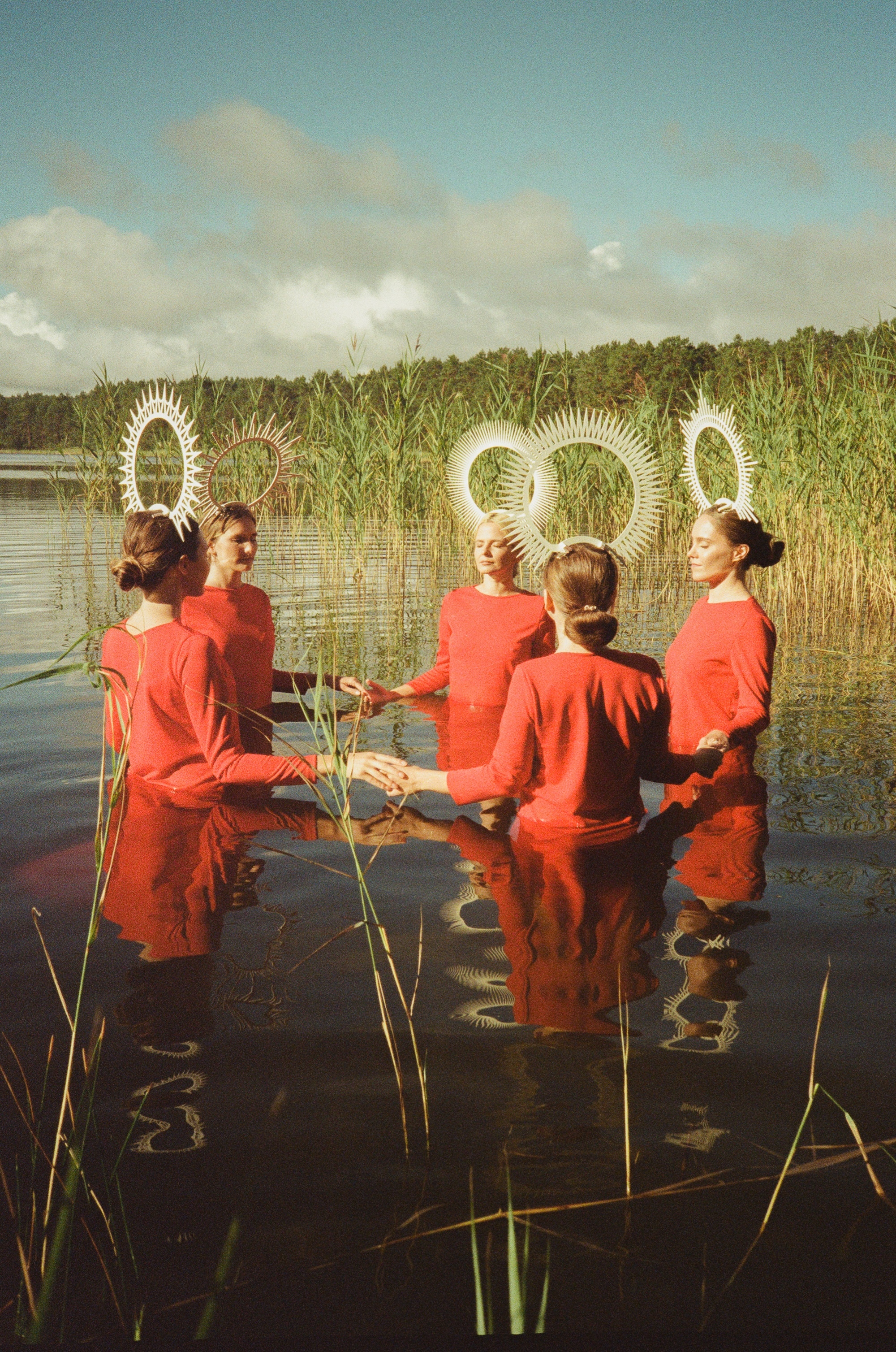 Group of figures in red outfits with illuminated halos, standing in a lake surrounded by reeds.