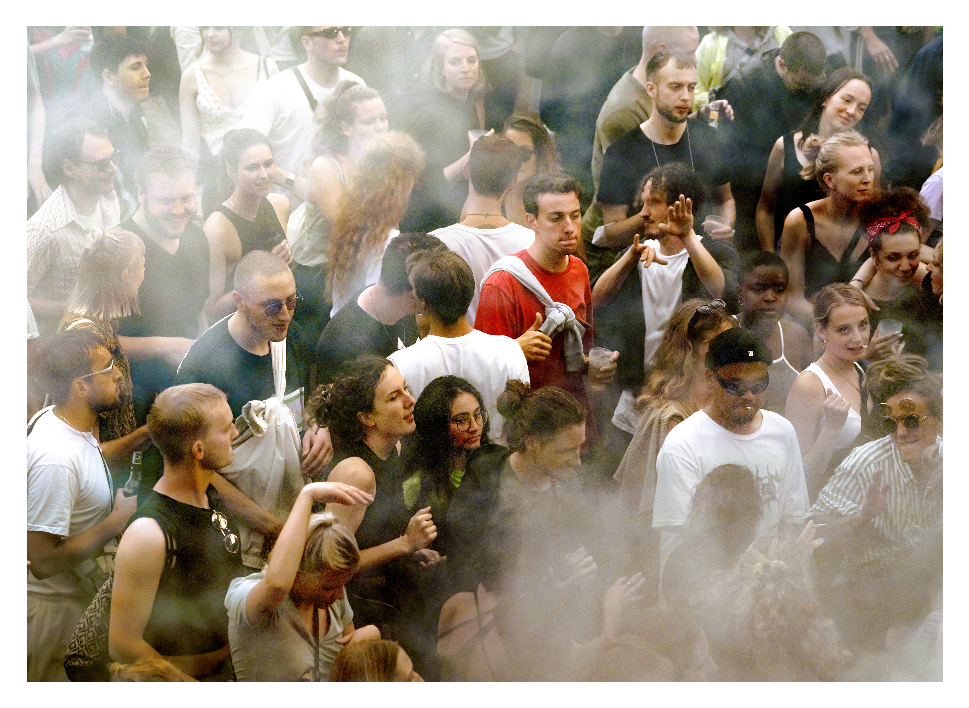 Large crowd of people in casual clothing with smoke or haze obscuring parts of the scene, creating a misty atmosphere.