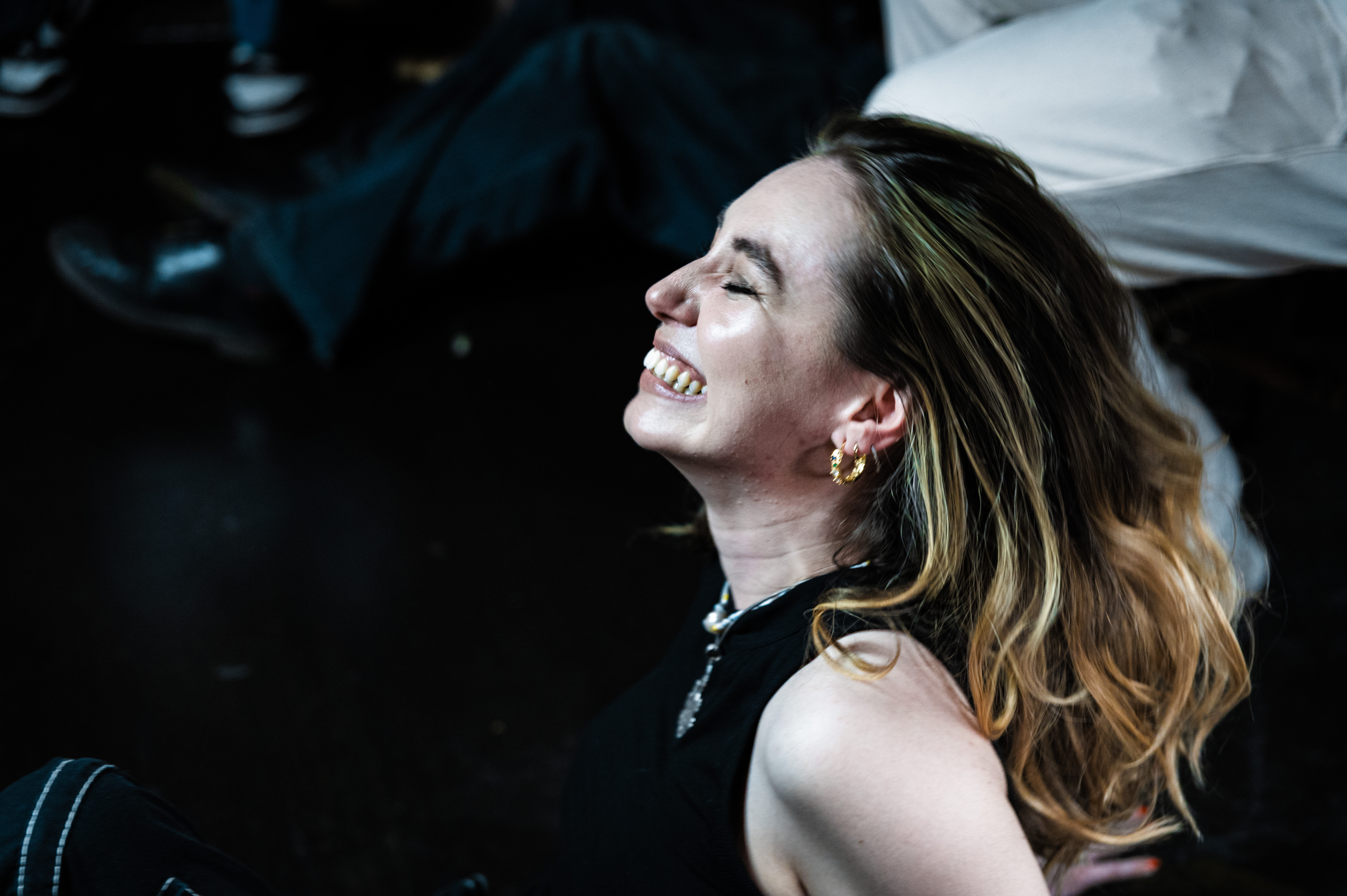 A woman with long, wavy, blonde hair smiling in a dimly lit setting.