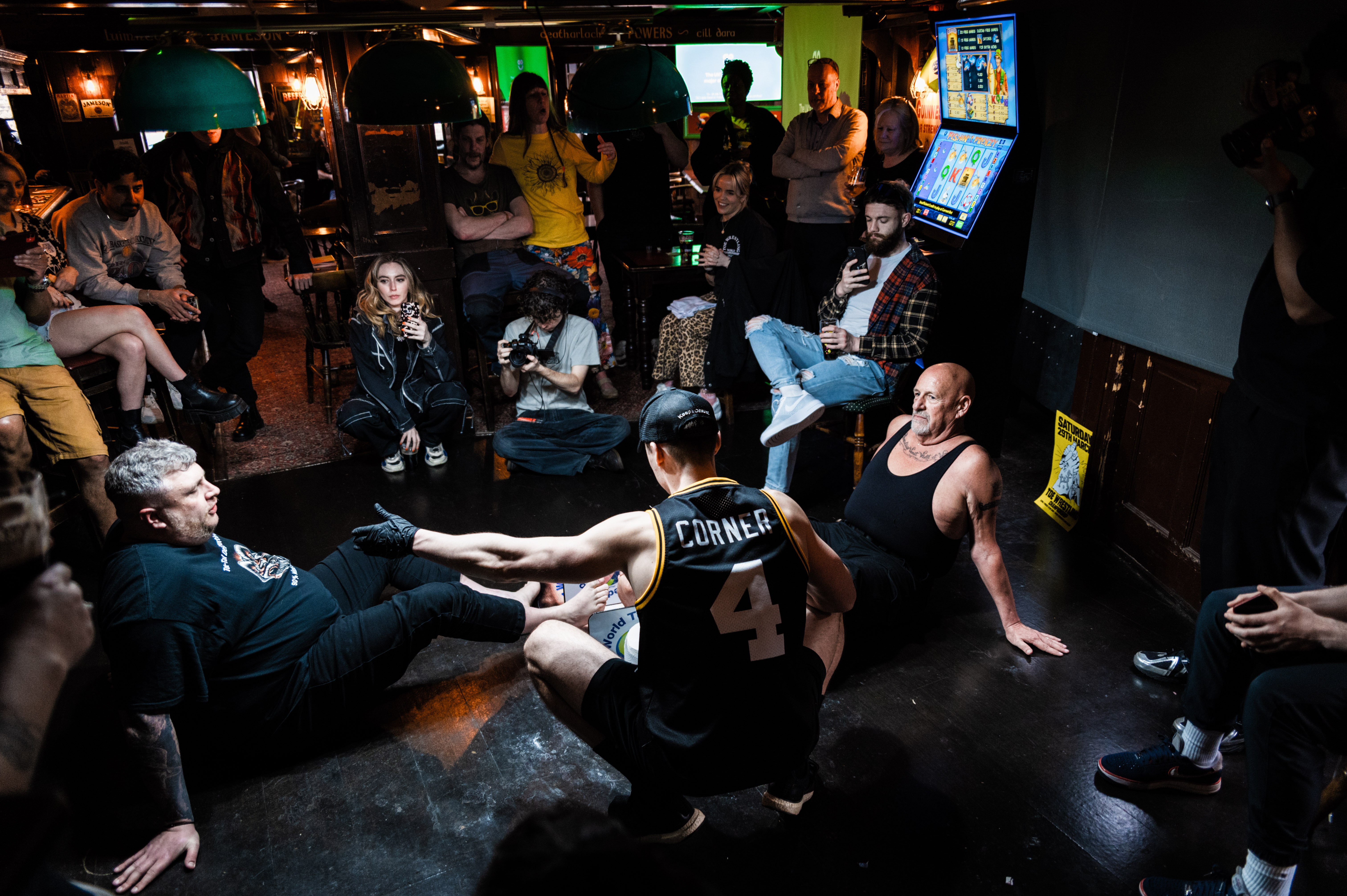 Crowded bar with people drinking, socialising, and playing arcade games.