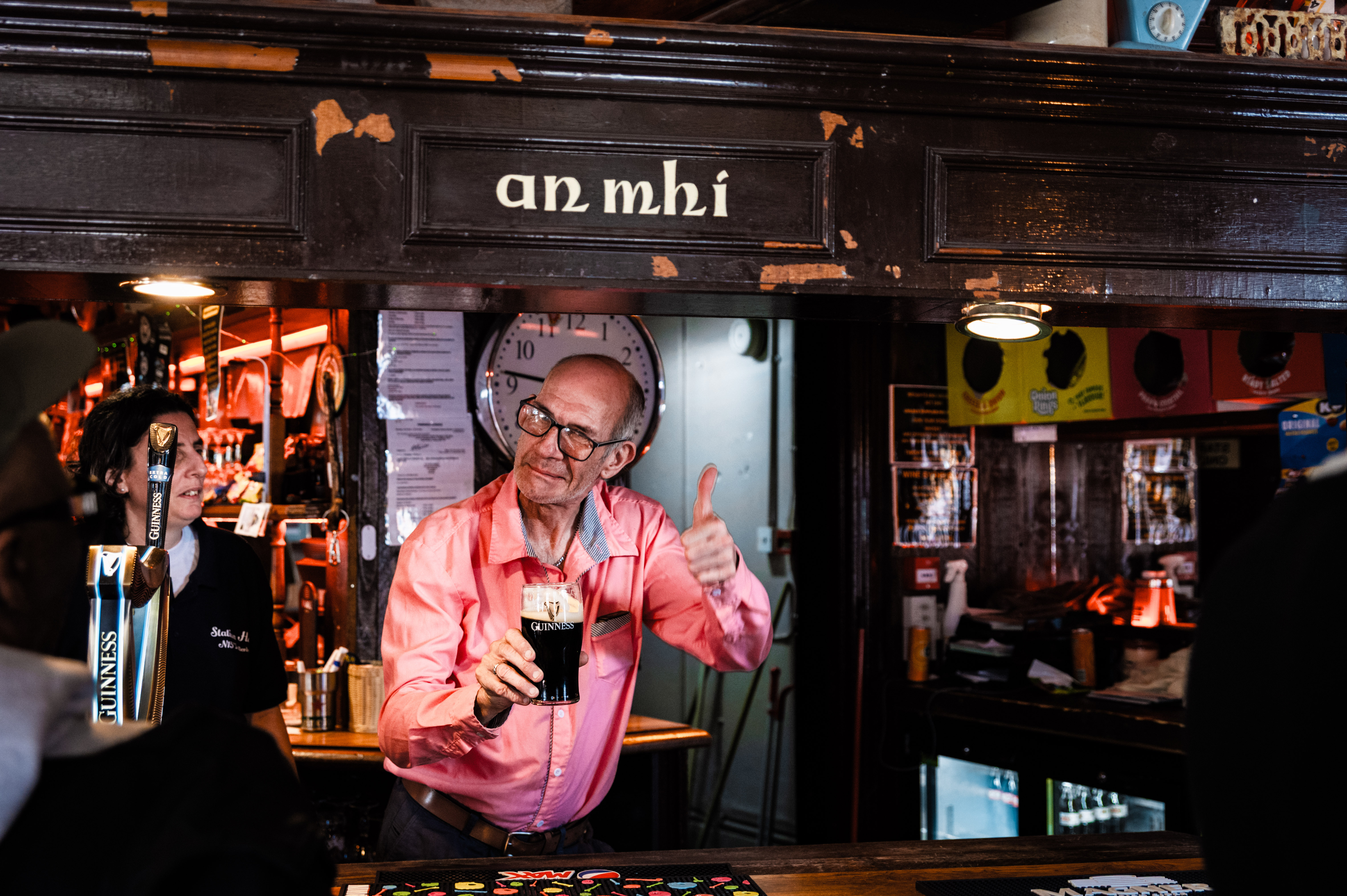 Elderly person in a busy bar, holding a drink and smiling.